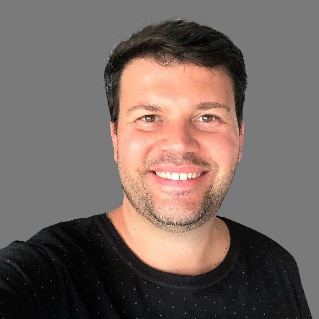 Um homem com barba está sorrindo e vestindo uma camisa preta.