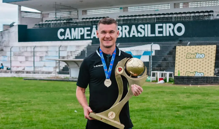 Um homem está segurando um troféu em um campo de futebol.