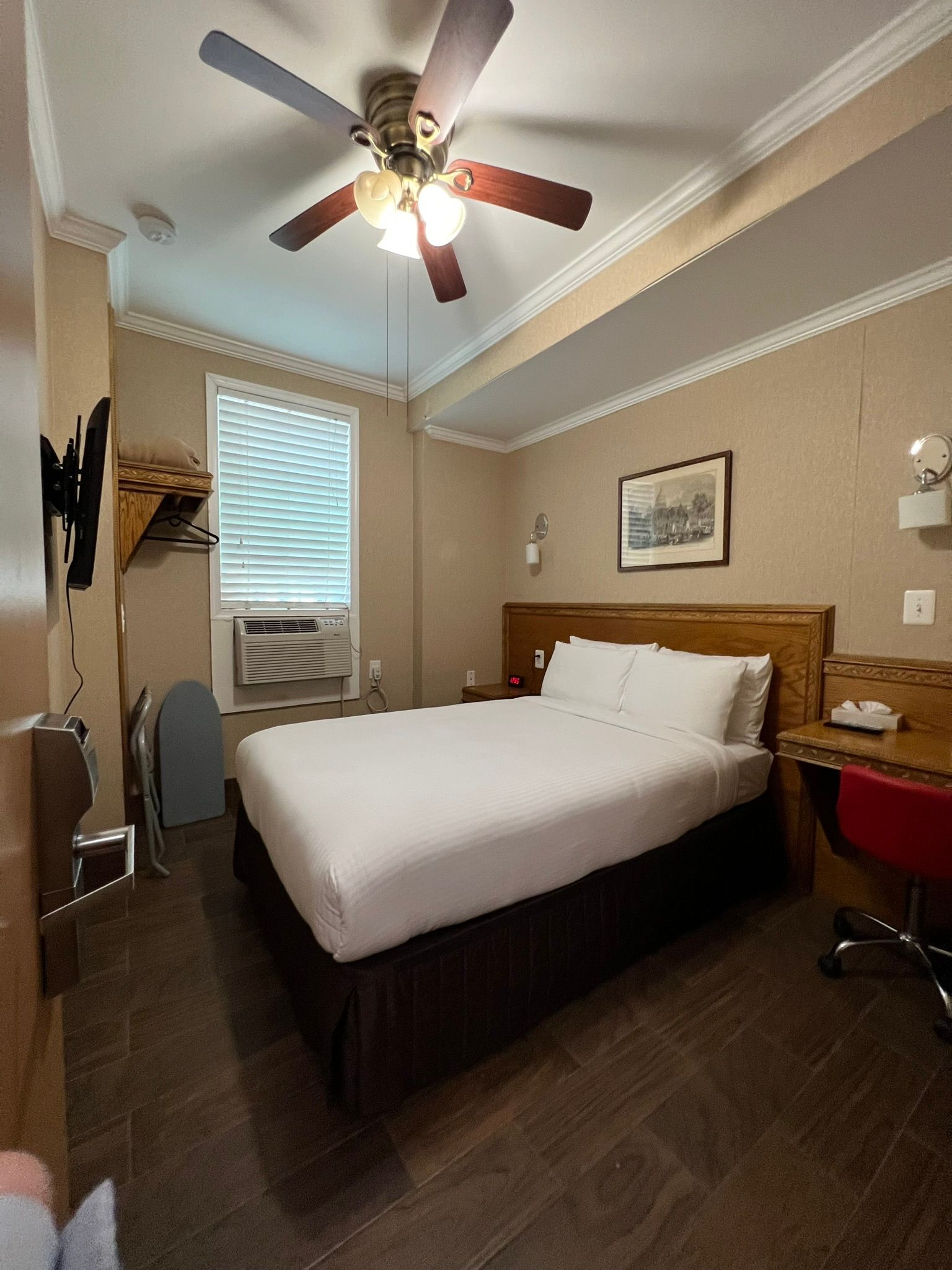 Bedroom with a double bed, desk, and window with blinds. Brown and beige color scheme, ceiling fan, and a framed picture.