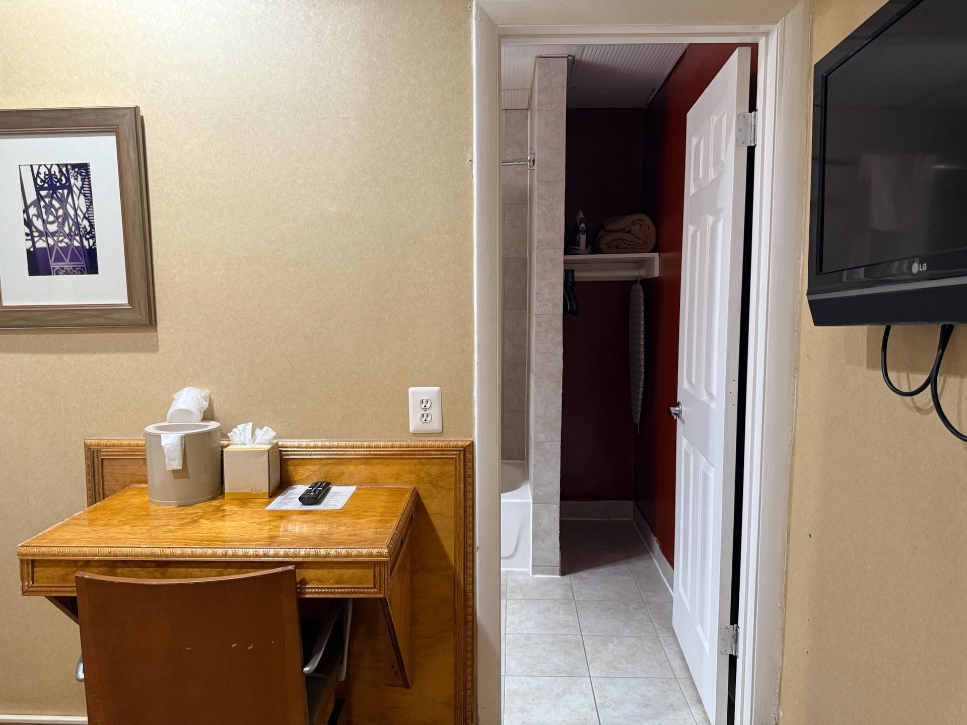 A hotel room interior with a desk, chair, and a doorway to the bathroom. The walls are tan, and the bathroom is painted red.