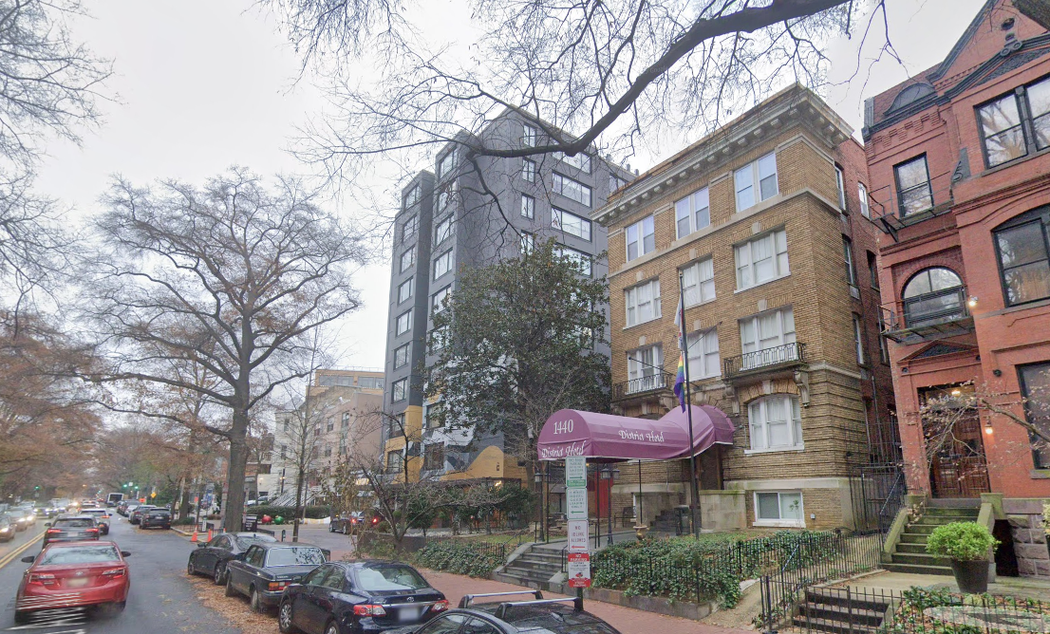 A row of cars are parked in front of a building with a purple awning.