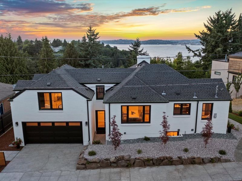 White house with black trim and a dark gray roof overlooking water at sunset.