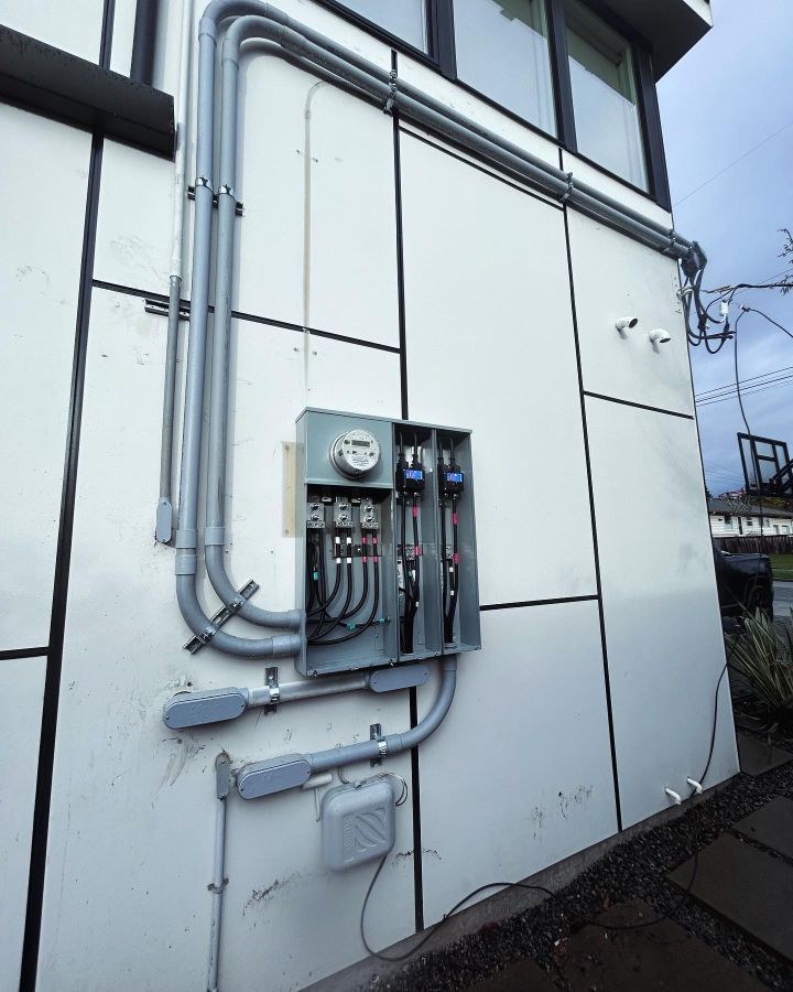 Exterior wall with utility meters, gray conduit, and electrical boxes on a white building.