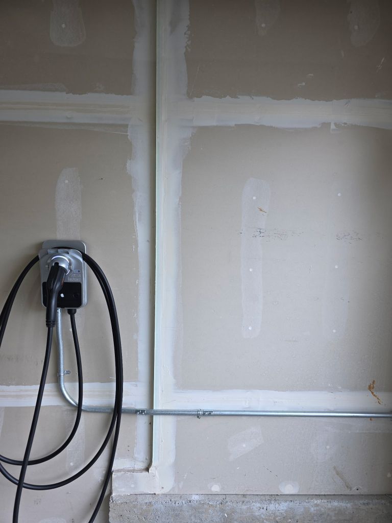 Garage wall with exposed cables and a mounted electrical box on unfinished drywall.