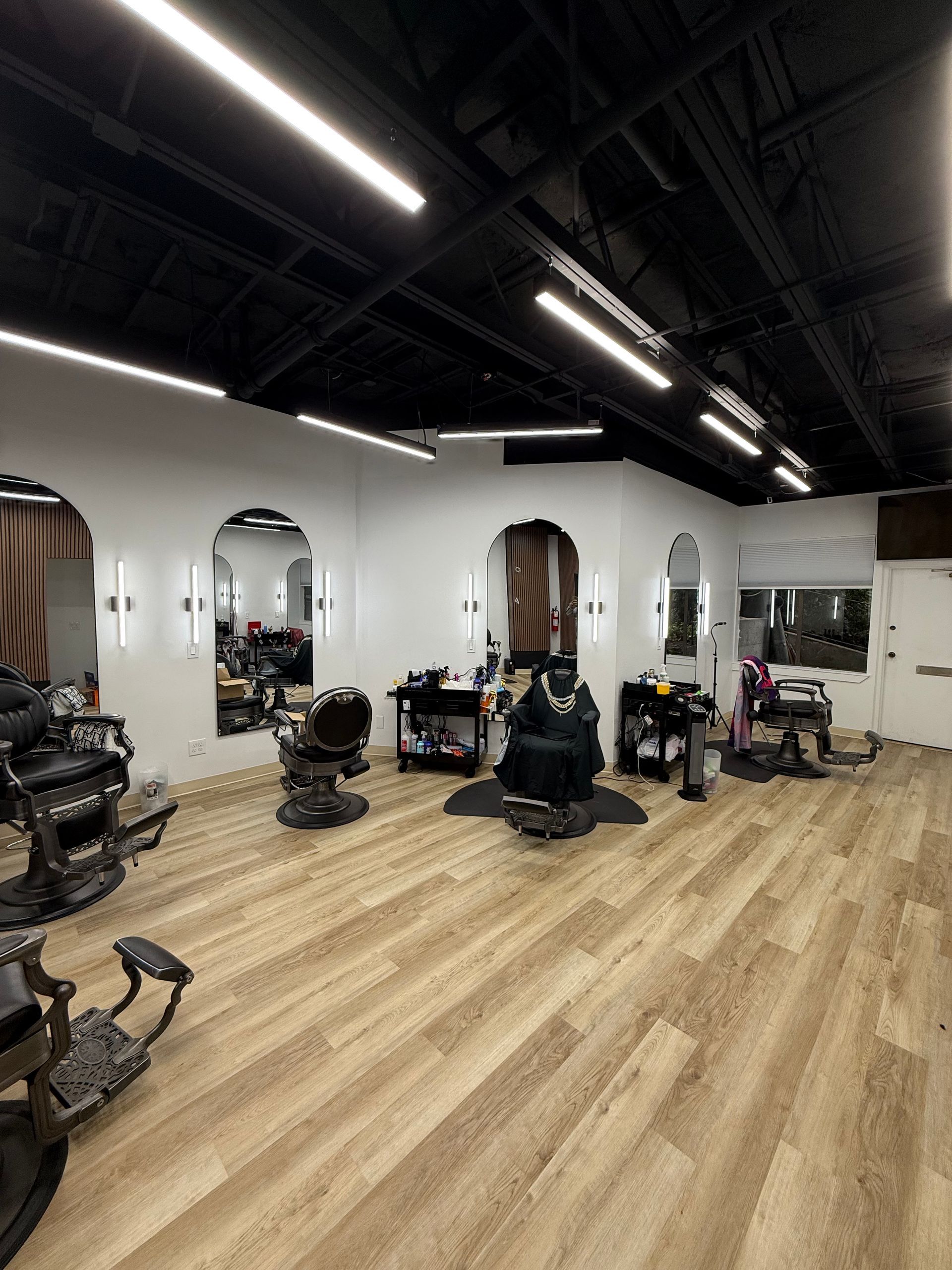 Modern barbershop with multiple chairs, mirrors, and black ceiling lights on a light wood floor