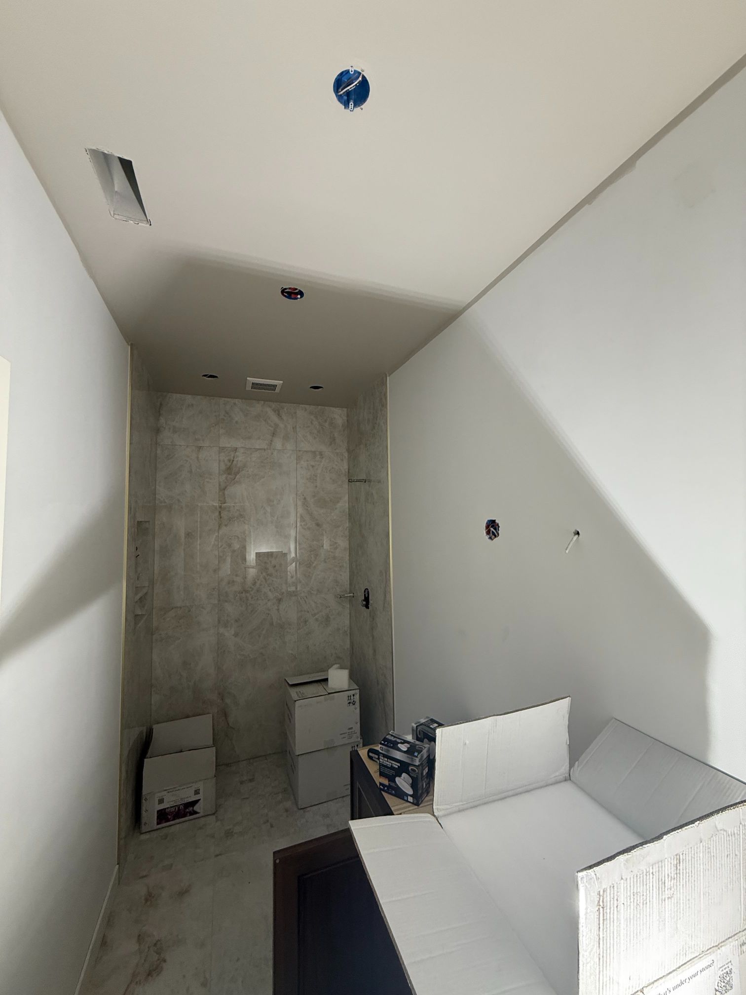 Narrow unfinished bathroom with white walls, gray tile shower, toilet, and a white bench or vanity.