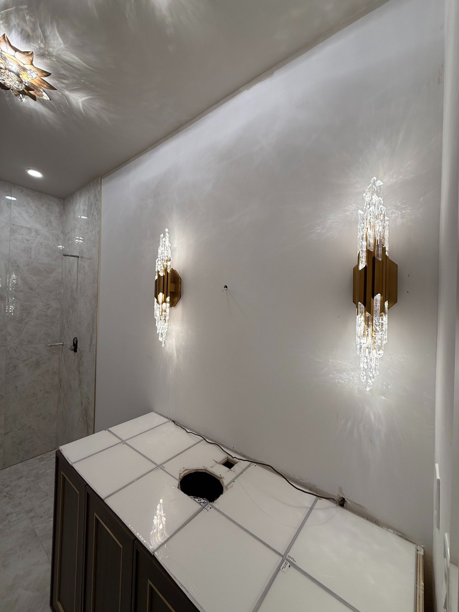 Modern bathroom vanity with white tile, dark cabinets, and gold wall sconces on a glossy wall
