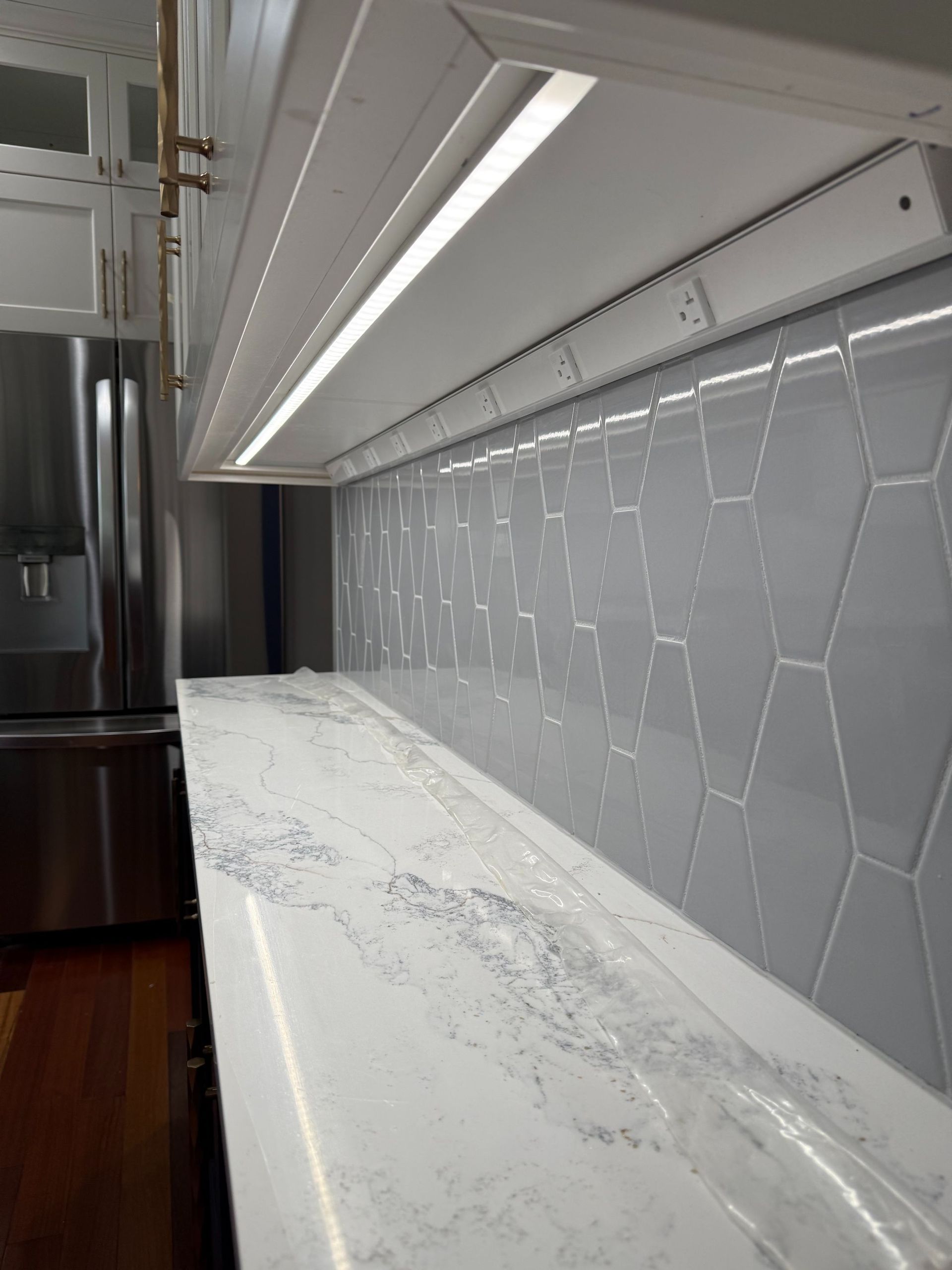 Empty modern kitchen counter with gray hex tile backsplash and under-cabinet lighting