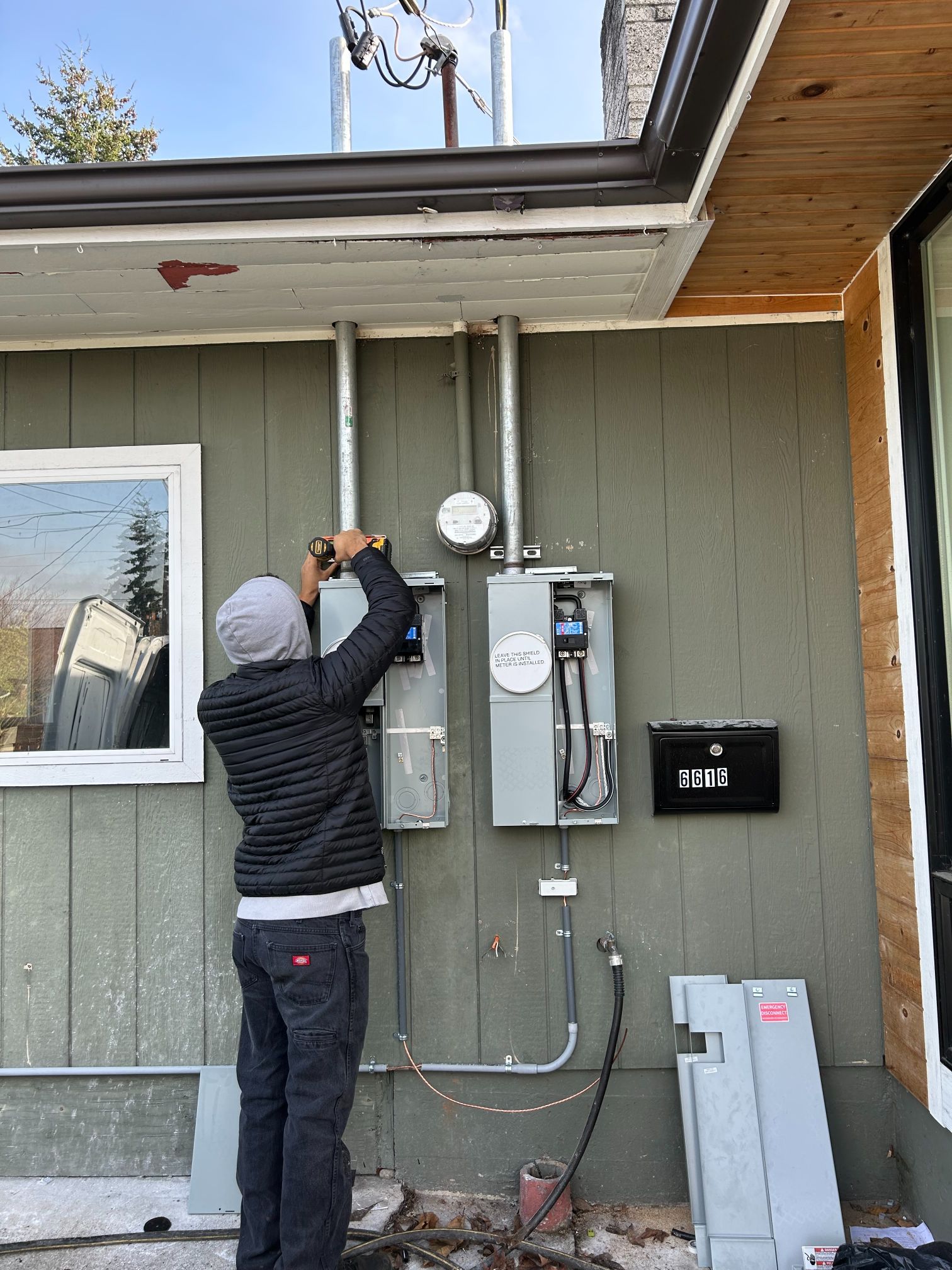 Person installing equipment on an exterior house wall beside electrical meters and conduit