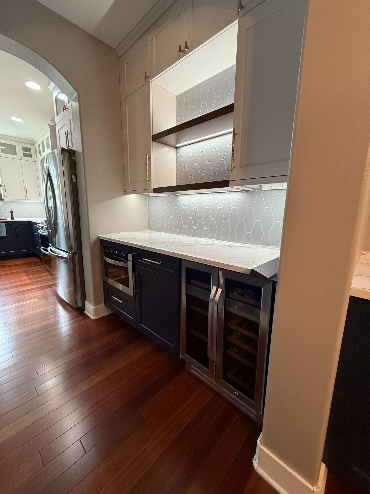 Modern kitchen with wood floors, white cabinets, marble countertop, and built-in wine fridge