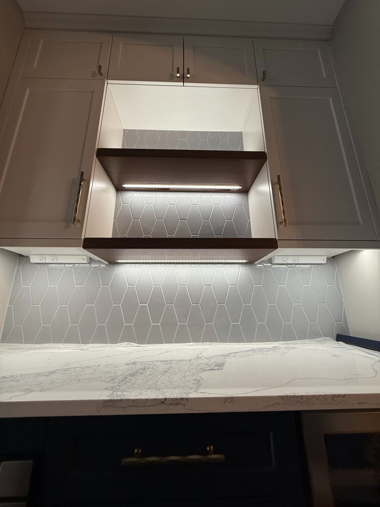 Modern kitchen with white cabinets, marble countertop, under-cabinet lighting, and stainless range hood