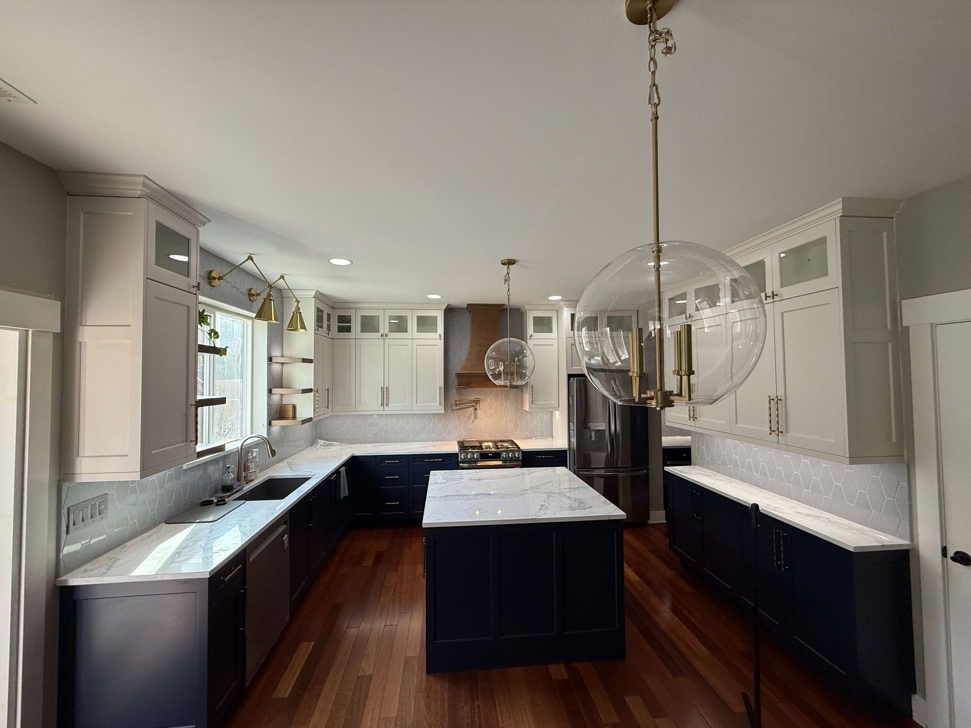 Bright kitchen with white cabinets, dark islands, and wood floors under pendant lights