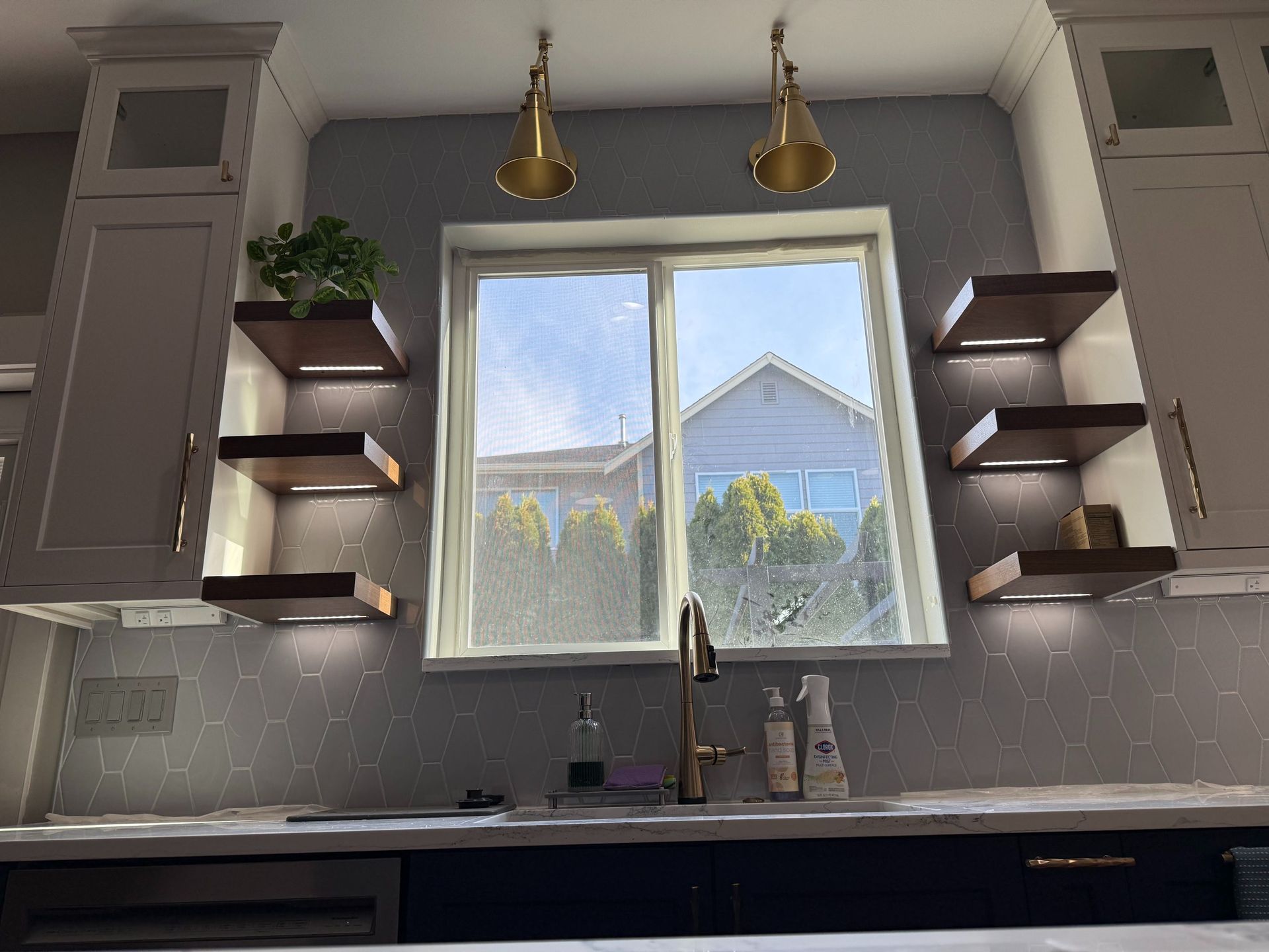 Modern kitchen with a window over the sink, floating shelves, and gray cabinets