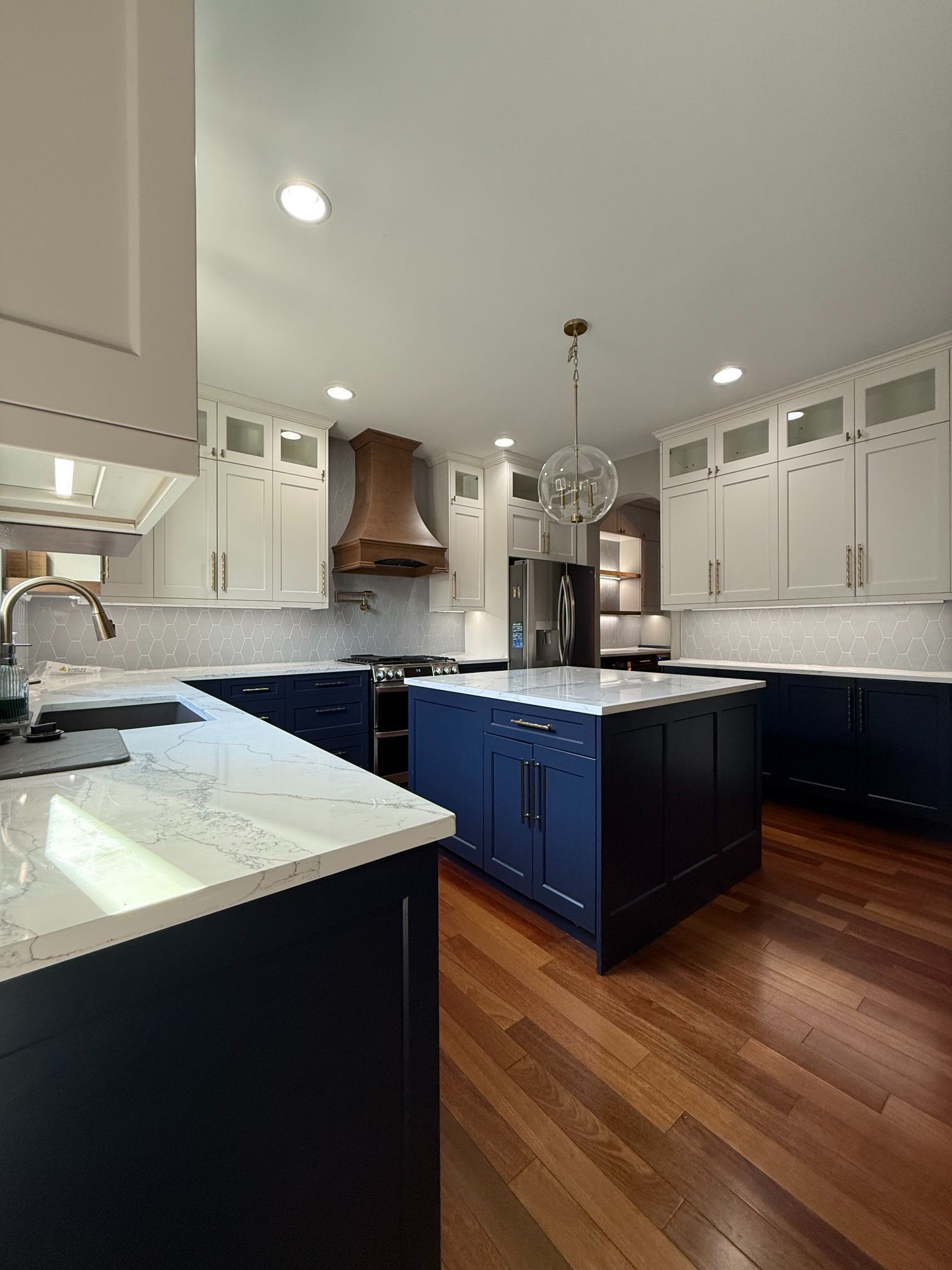 Bright modern kitchen with blue island, white cabinets, marble counters, and hardwood floors