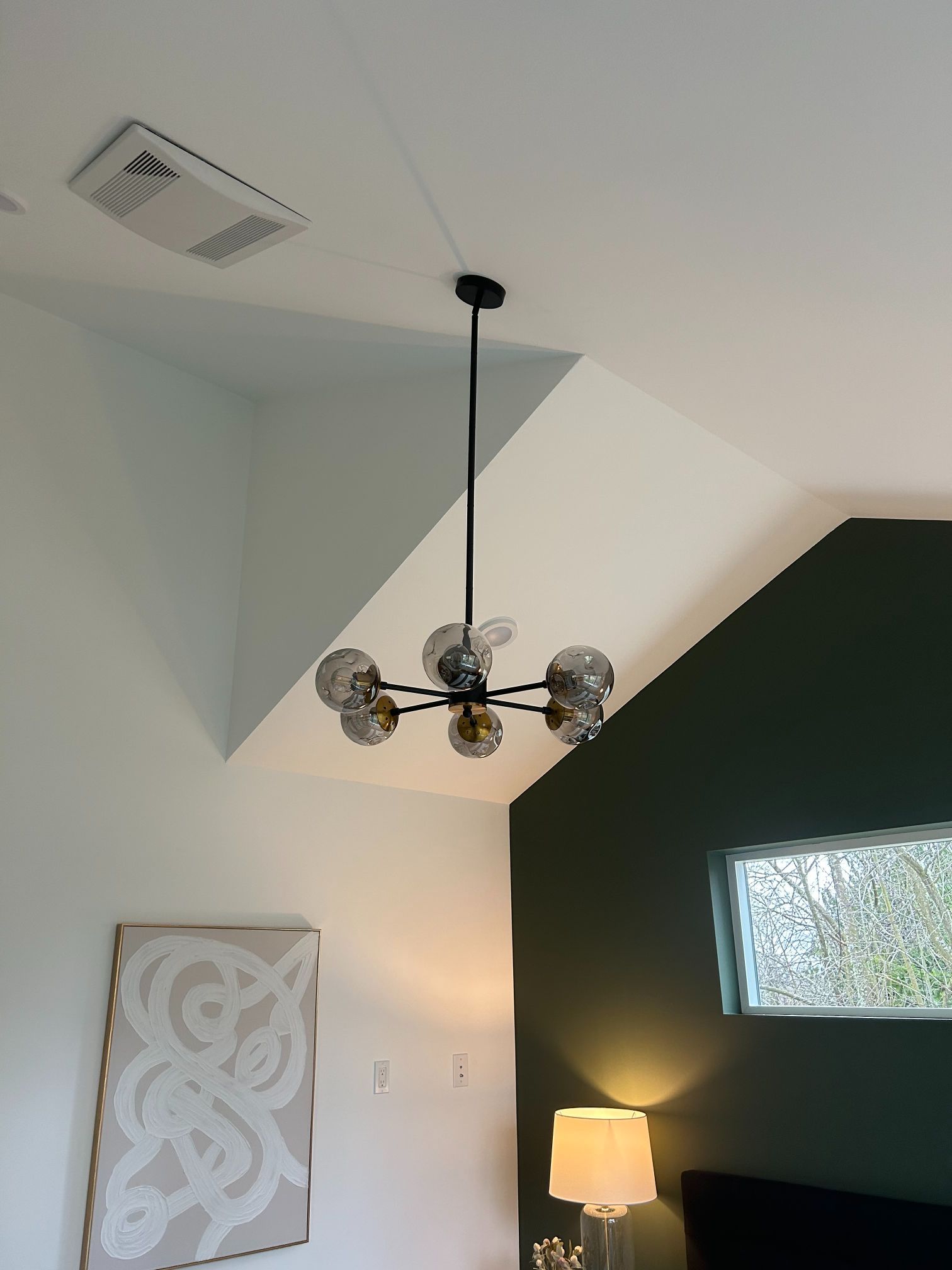 Modern interior with vaulted white ceiling, black accent wall, chandelier, floor lamp, and decorative wall art