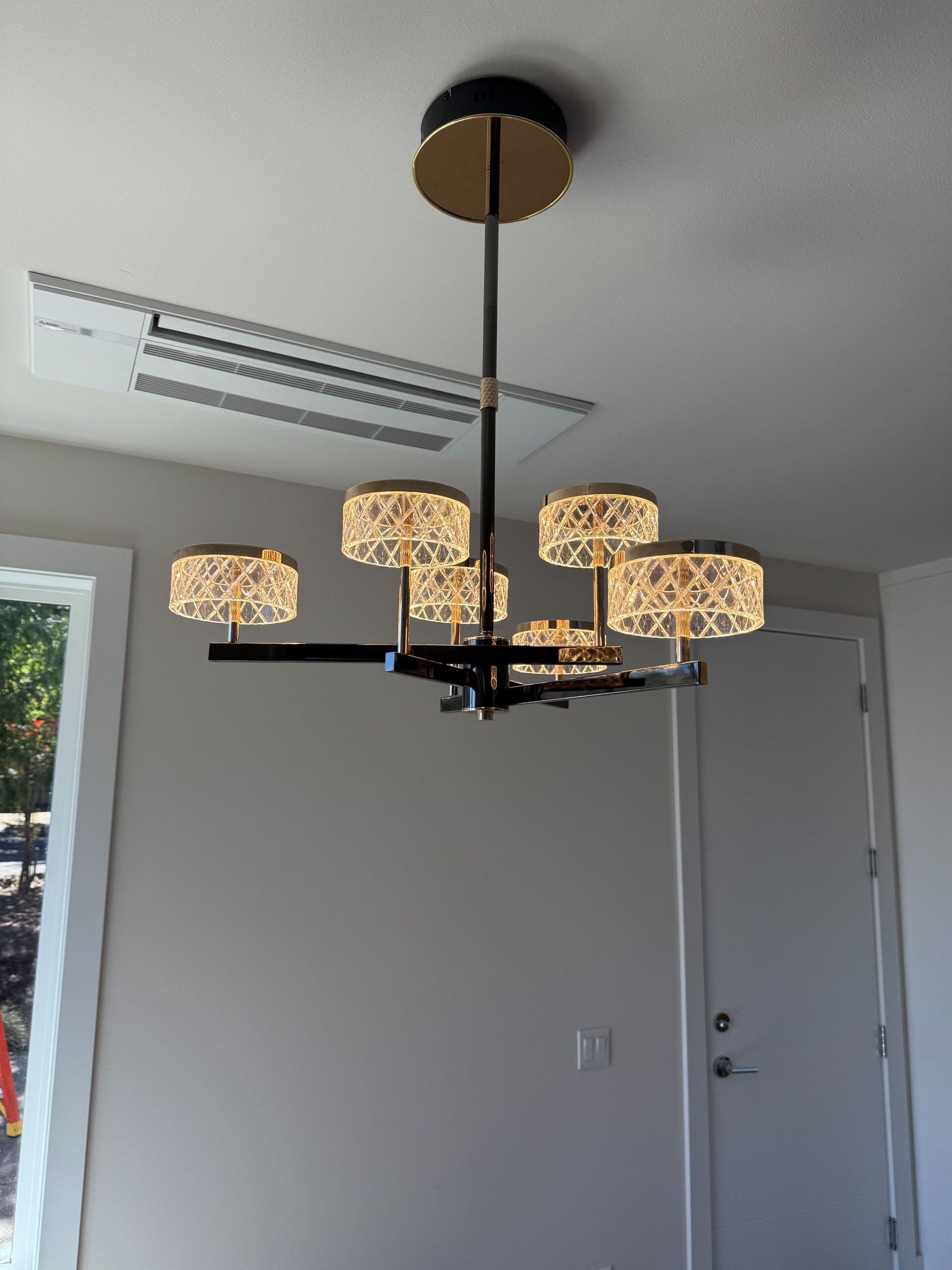 Modern black chandelier with beige patterned shades hanging in a gray room near a window and door