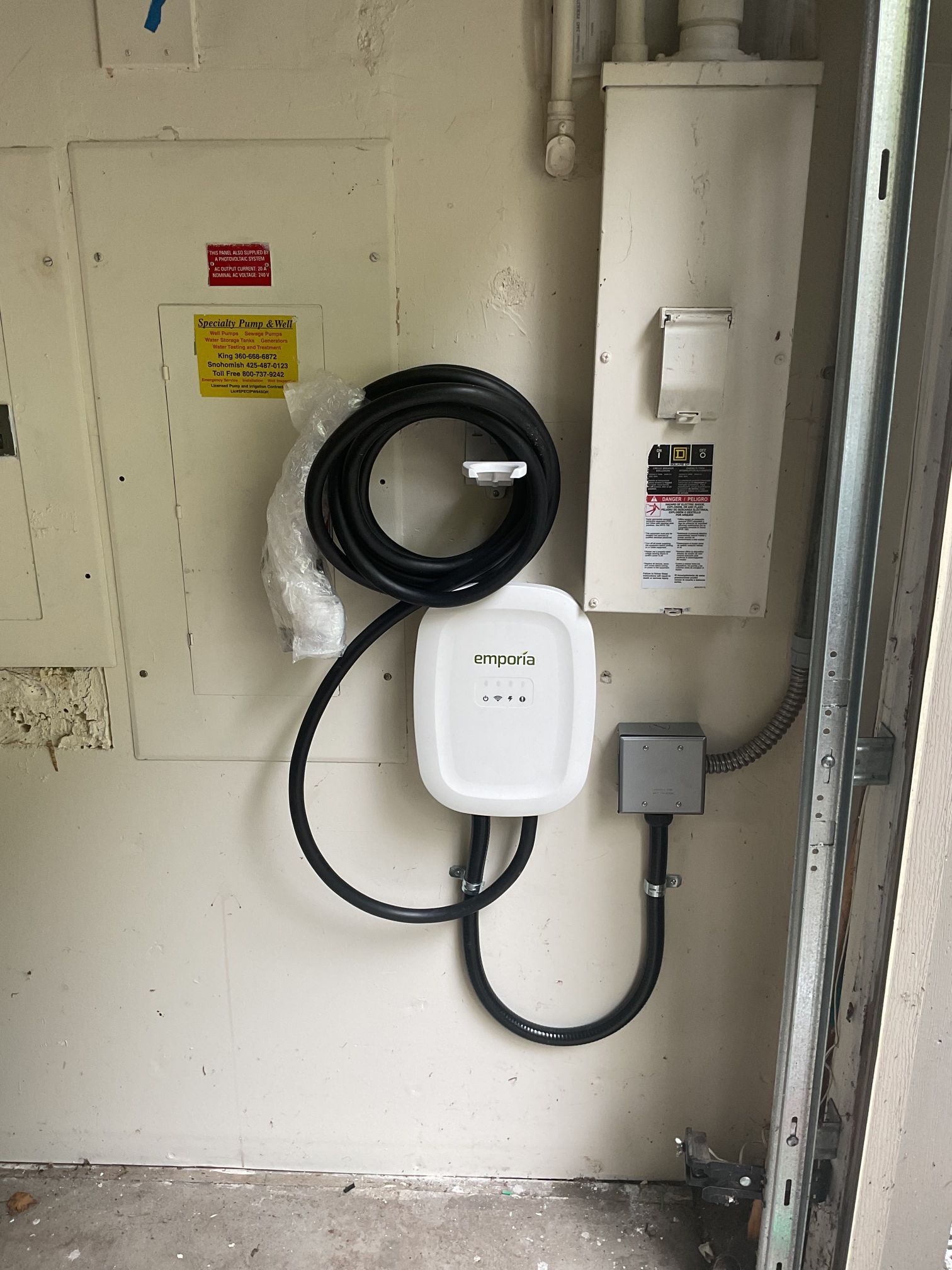 Wall-mounted utility equipment with coiled black cable, white box, and electrical conduit in a service area.