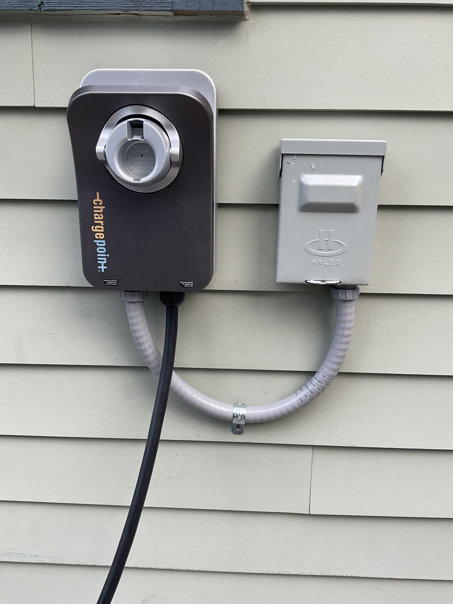 Outdoor EV charging station and gray electrical box mounted on a house siding.
