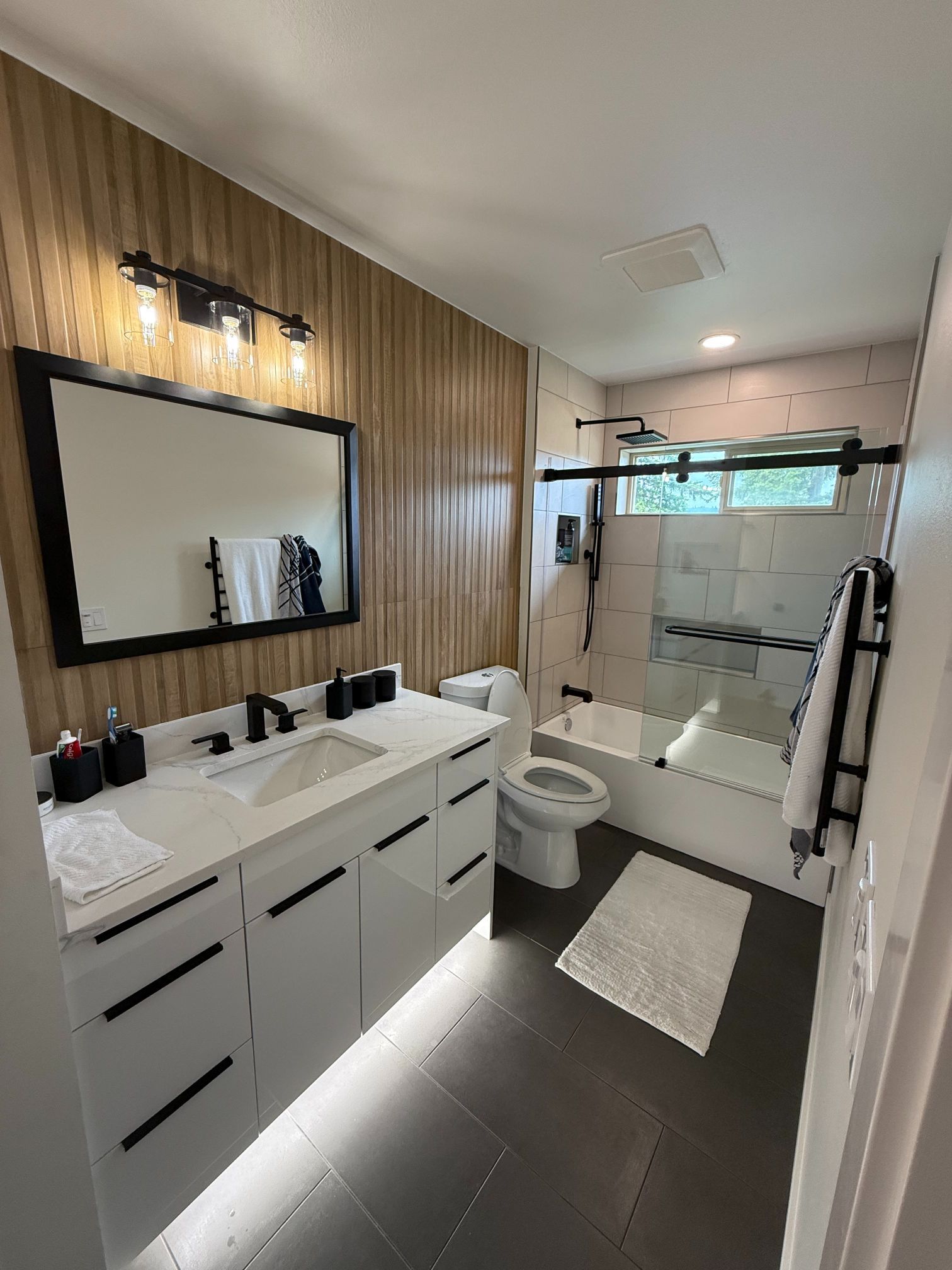 Modern bathroom with double vanity, large mirror, toilet, and glass shower with frosted window.