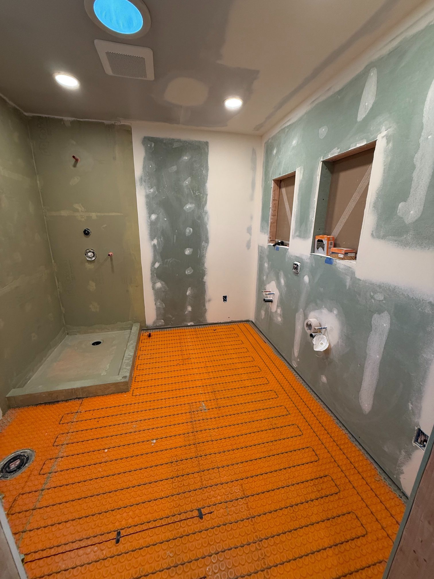 Partially finished bathroom with green drywall, orange floor membrane, and a shower stall under construction