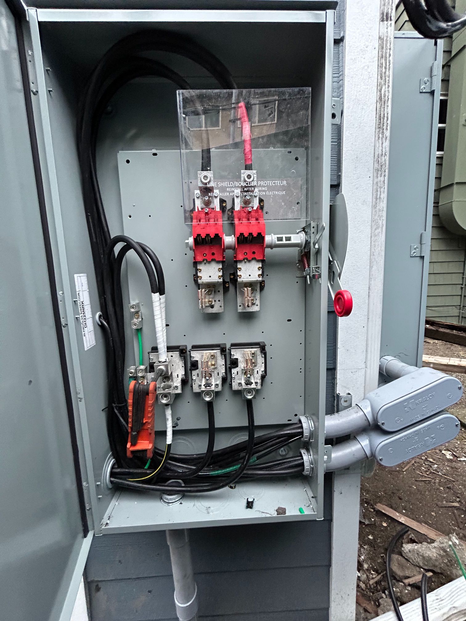 Open electrical control panel with red breakers and wiring in a metal cabinet outdoors