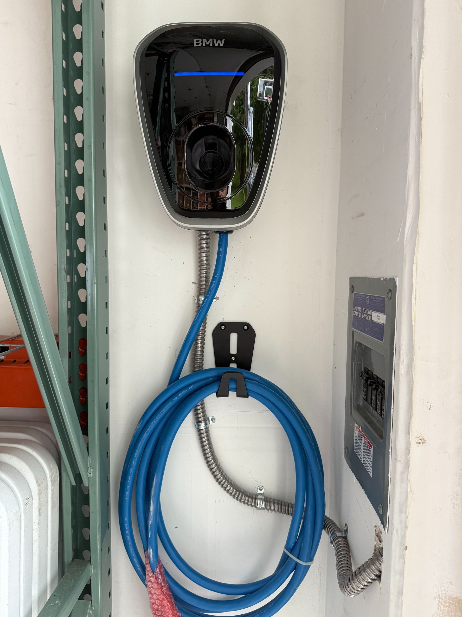 Wall-mounted black charging unit with a blue coiled cable beside a gray electrical panel.