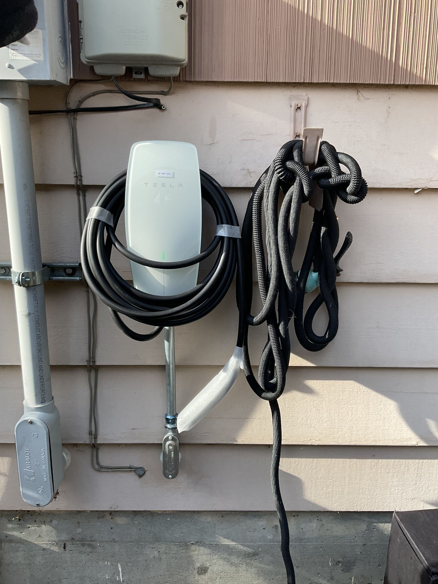 Coiled cables hanging on an exterior wall beside utility pipes and a gray electrical box