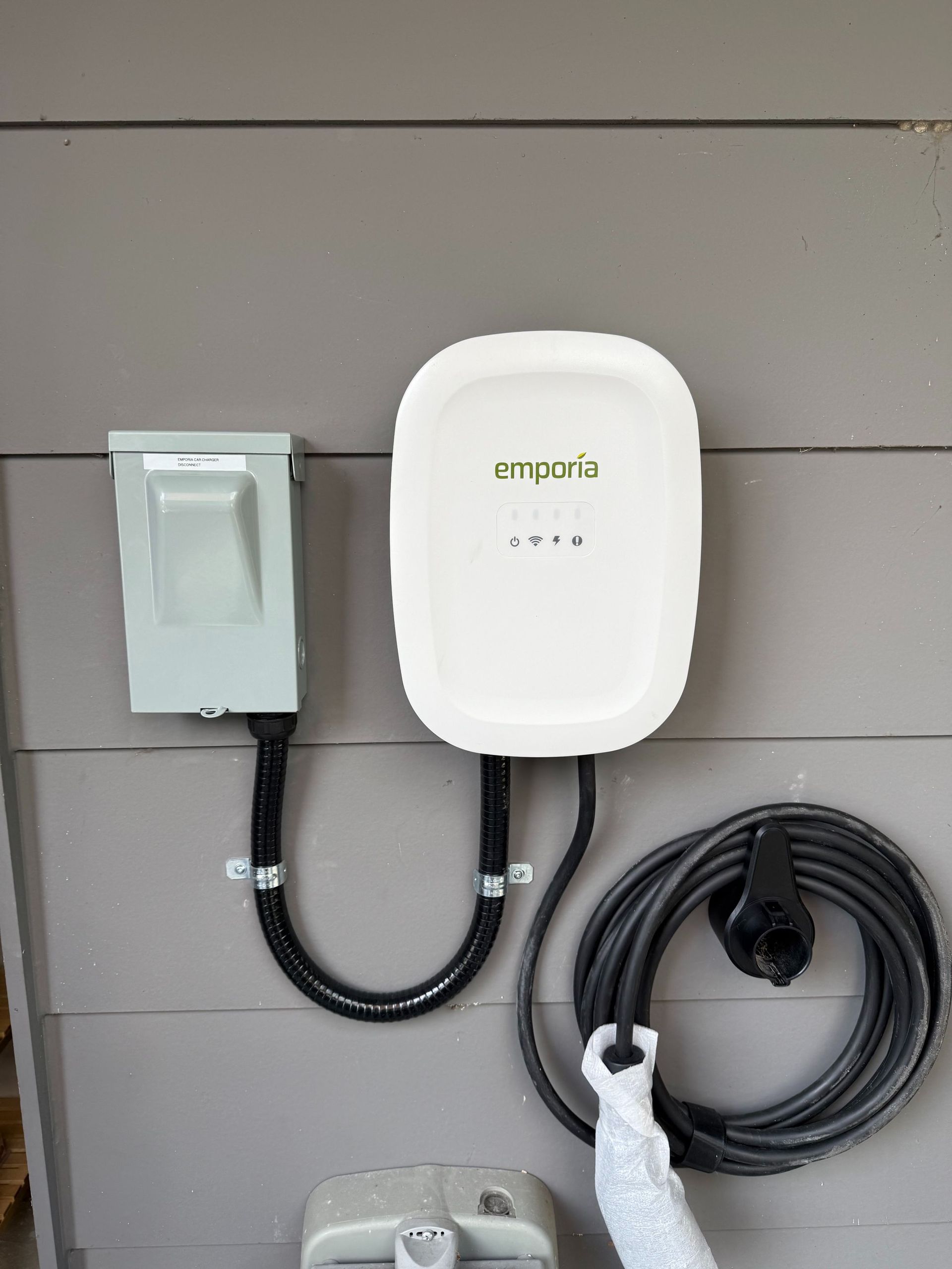 White Enphase solar inverter and gray electrical box mounted on a house exterior wall, with coiled cable.