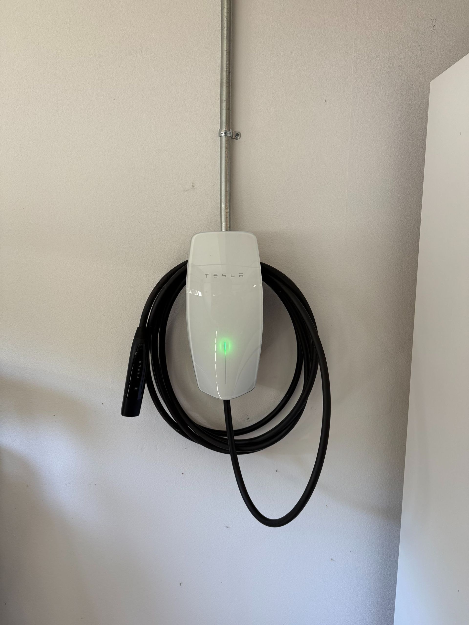White wall-mounted device with a green light and coiled black cable beside it