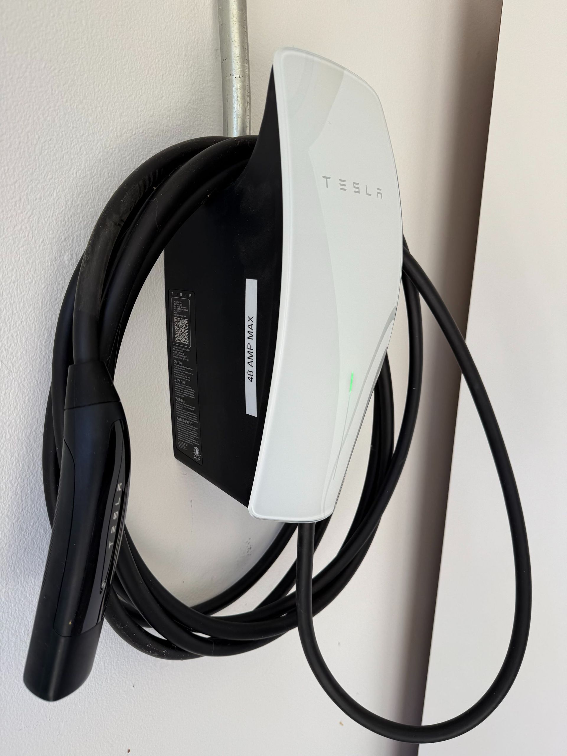 White wall-mounted EV charging unit with a coiled black cable and connector hanging beside it