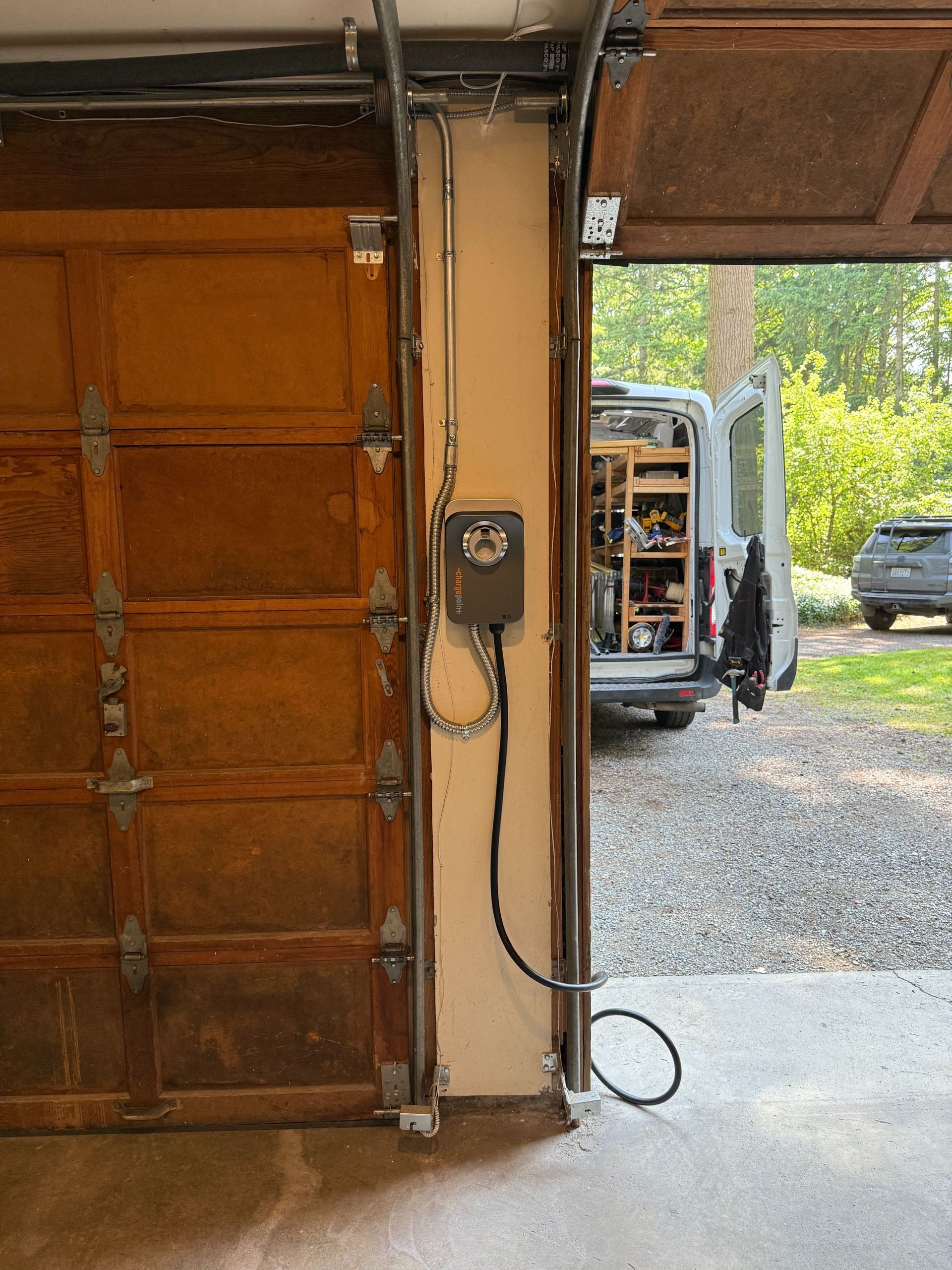 Garage doorway with a utility van outside on a gravel driveway, and a yellow car in the background.