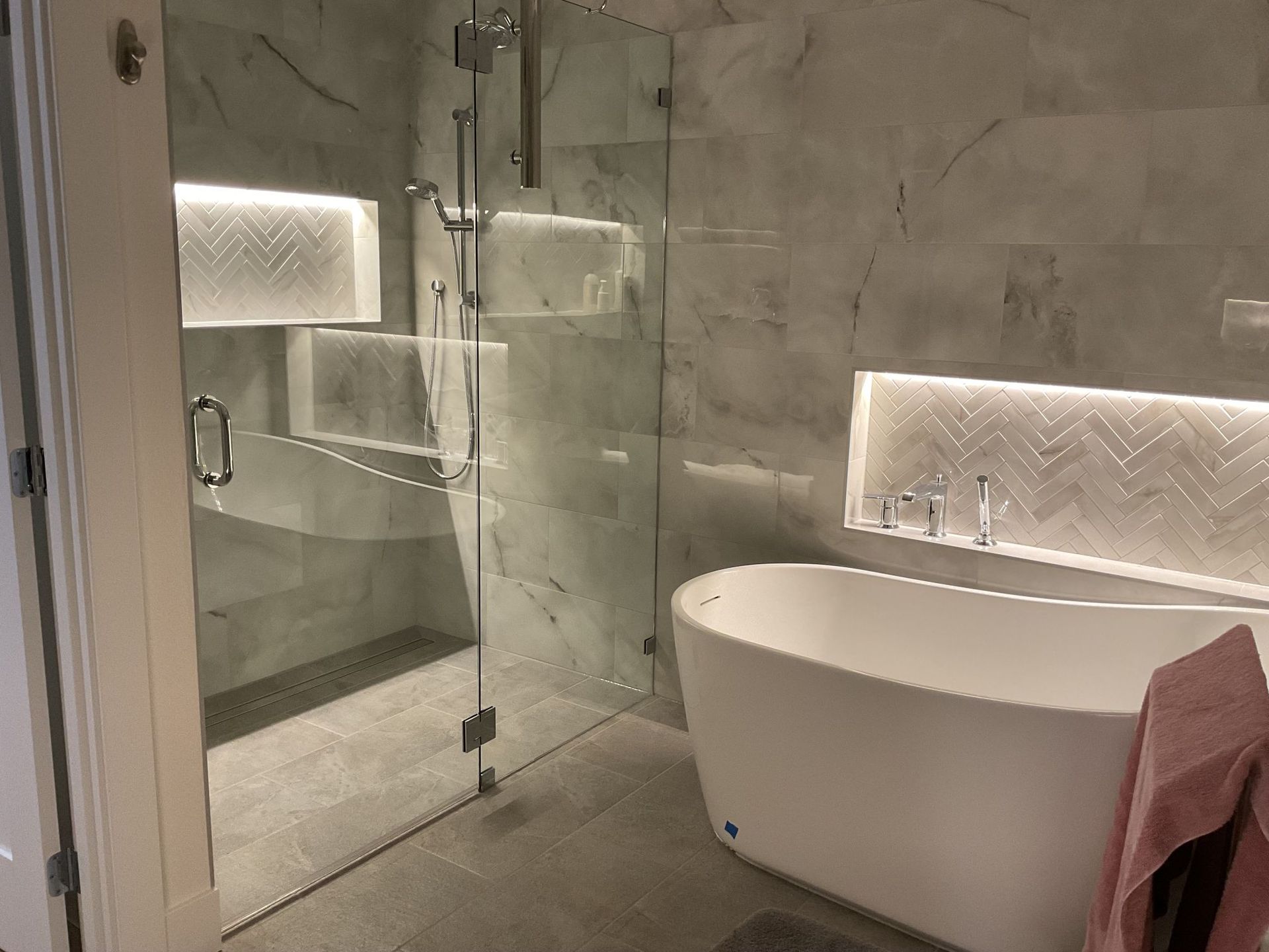 Modern bathroom with glass shower, freestanding tub, and illuminated wall niches
