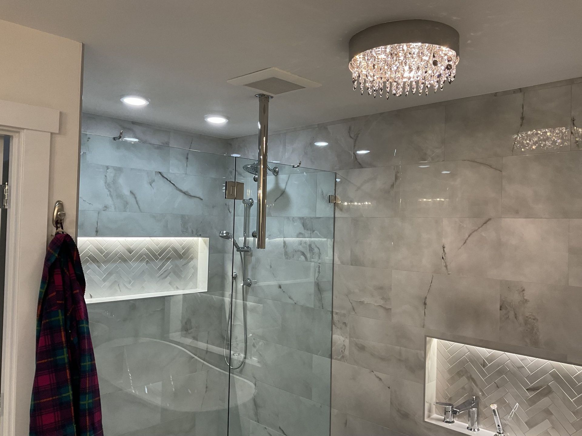 Modern bathroom with gray marble walls, glass shower, and crystal ceiling light