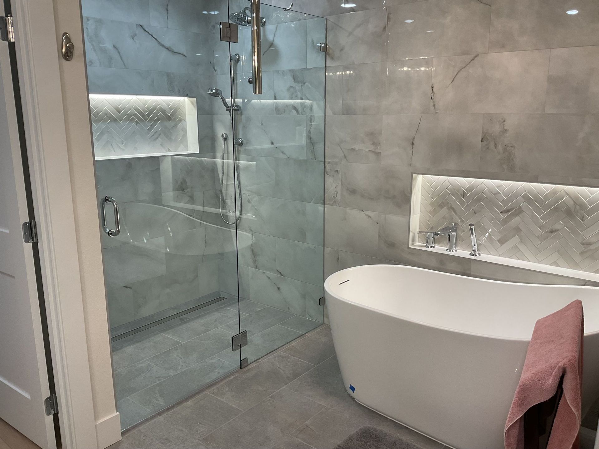 Modern bathroom with glass shower, freestanding tub, and gray tile flooring