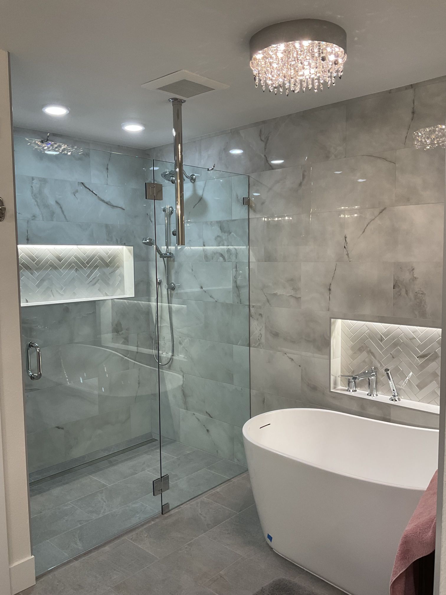 Modern gray-tiled bathroom with glass shower, freestanding tub, and crystal ceiling light