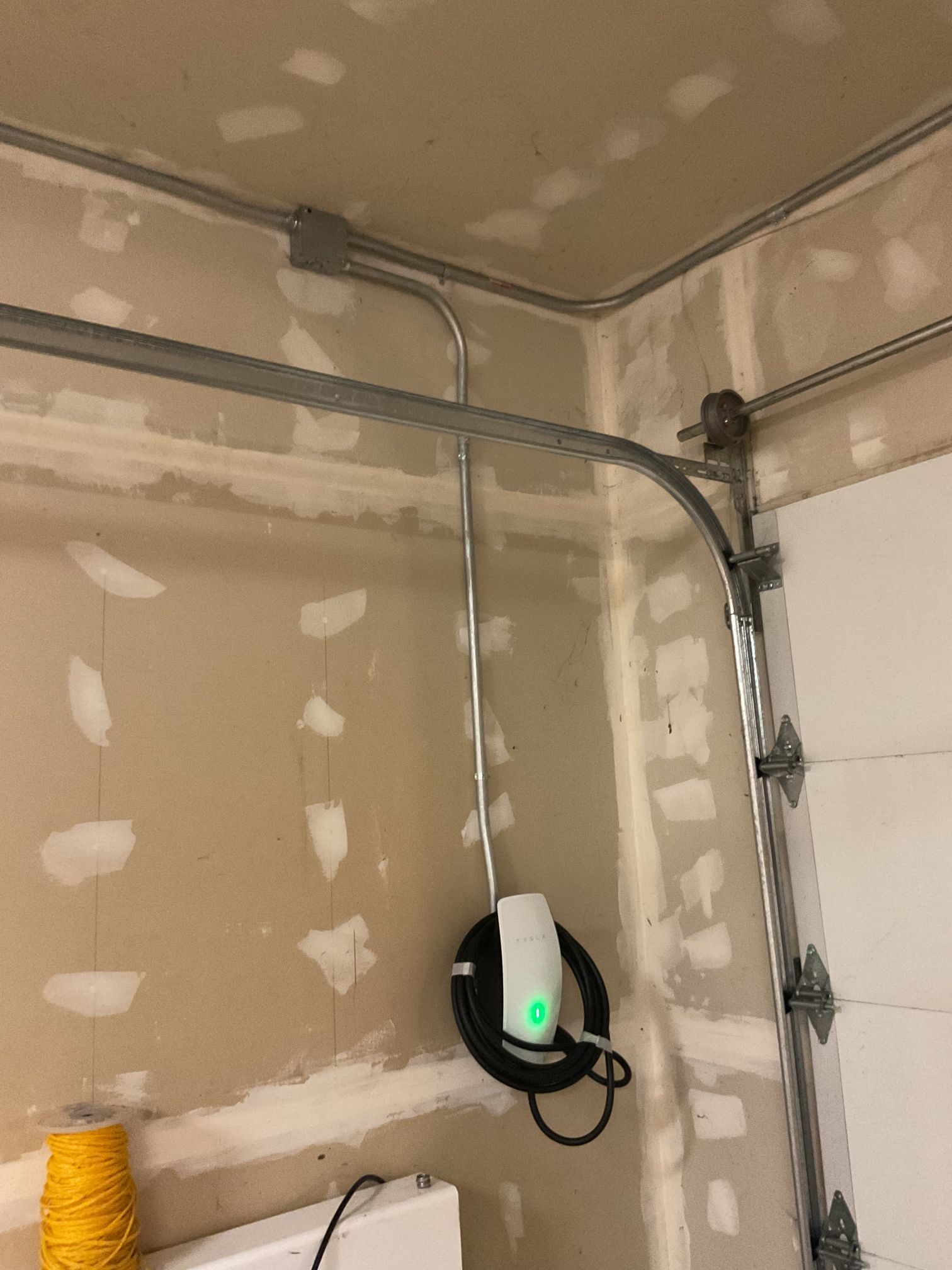 Garage wall with mounted EV charger and conduit in an unfinished room.