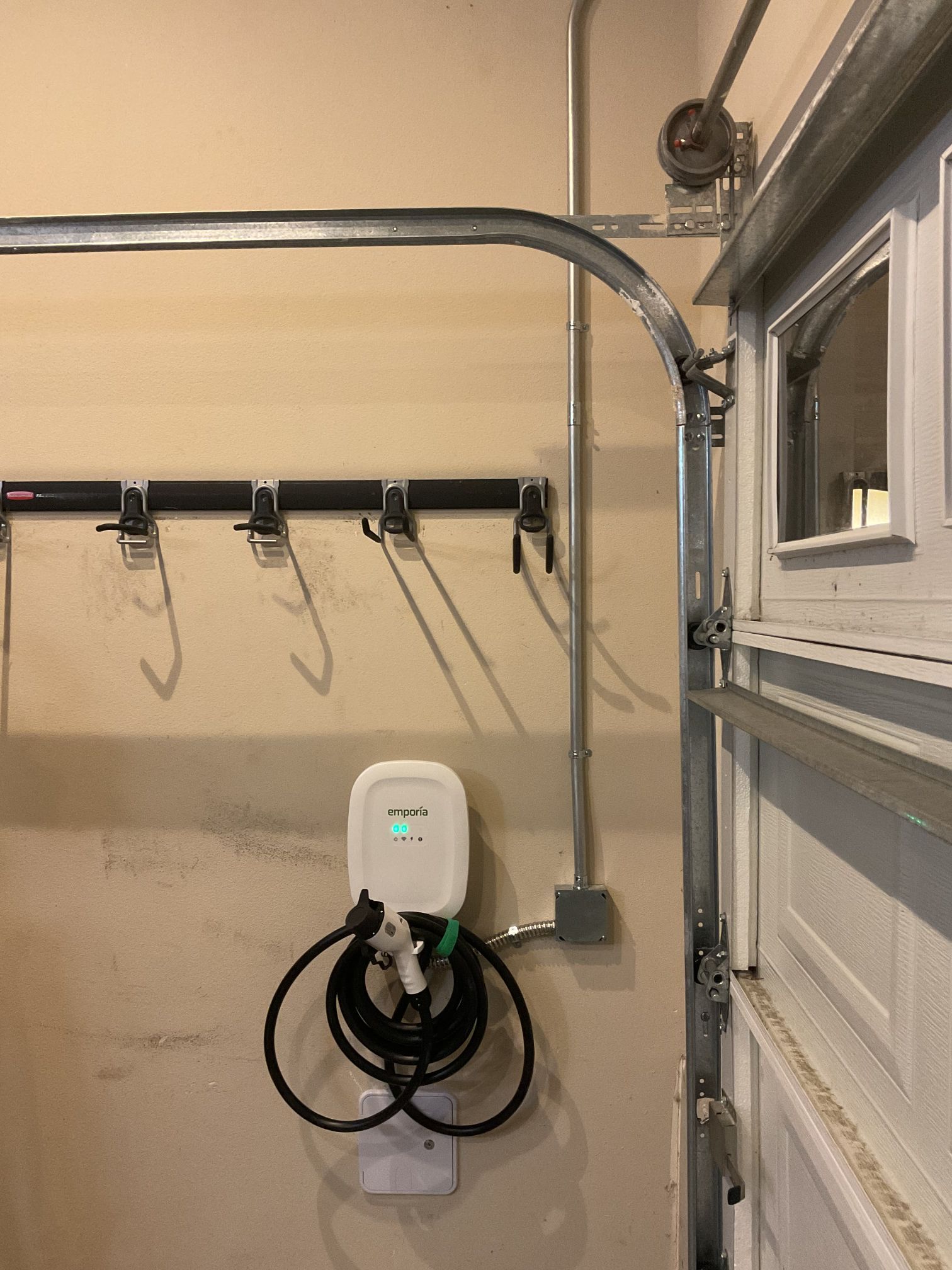 Wall-mounted EV charger in a garage next to hooks and a garage door.