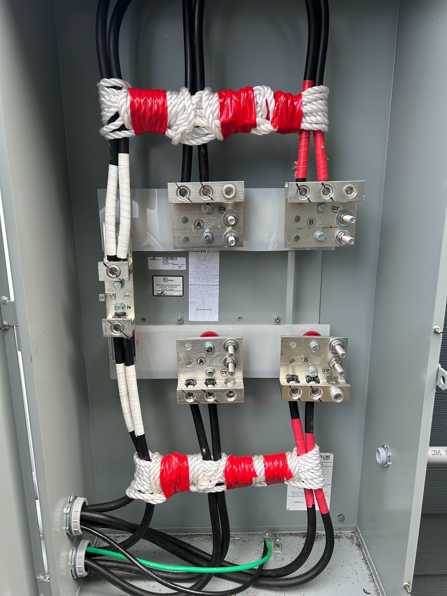 Open electrical panel with red and white insulated bus bars and wiring blocks inside a gray cabinet
