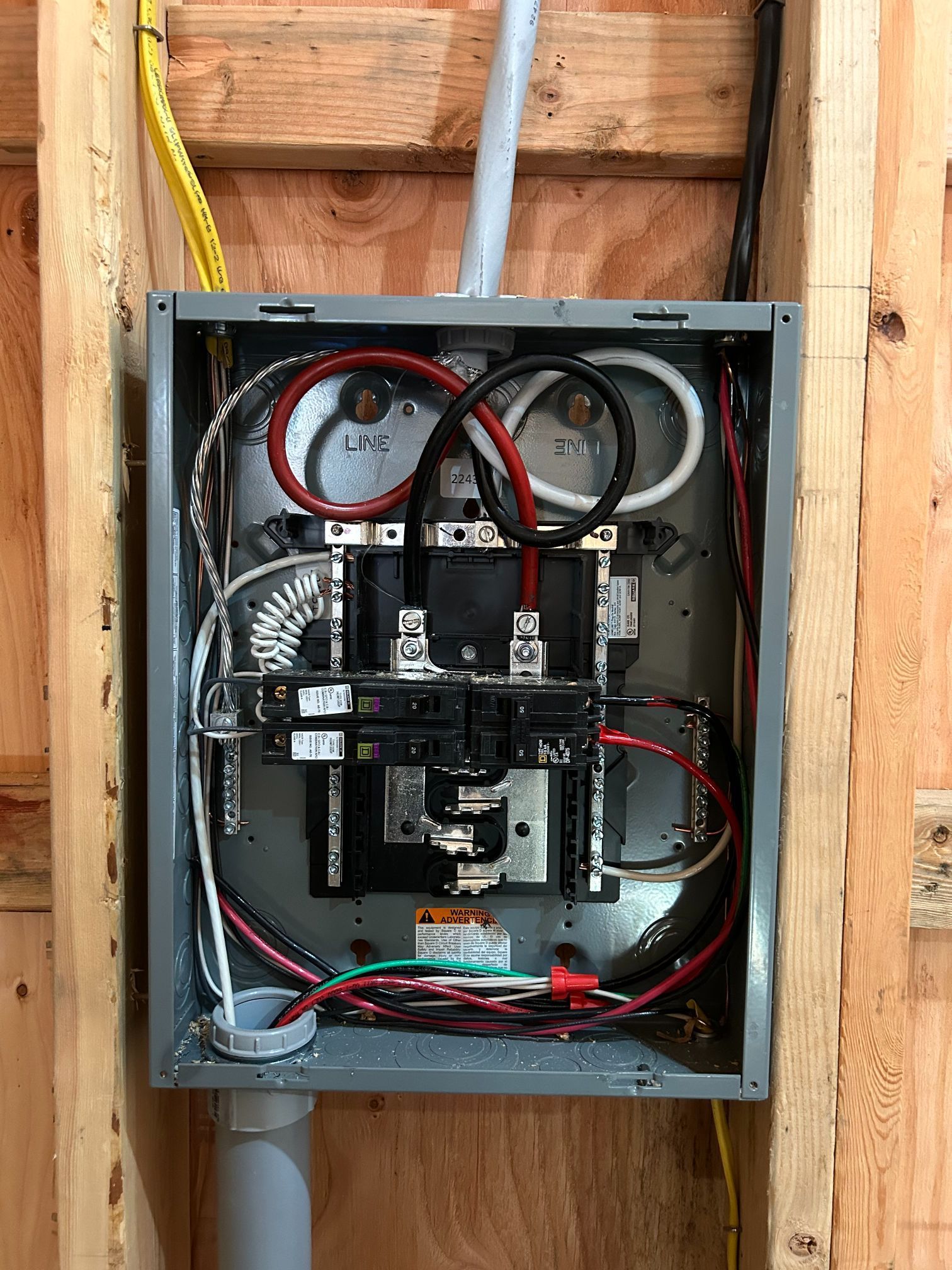 Open electrical panel with wiring and breakers mounted between exposed wooden studs.