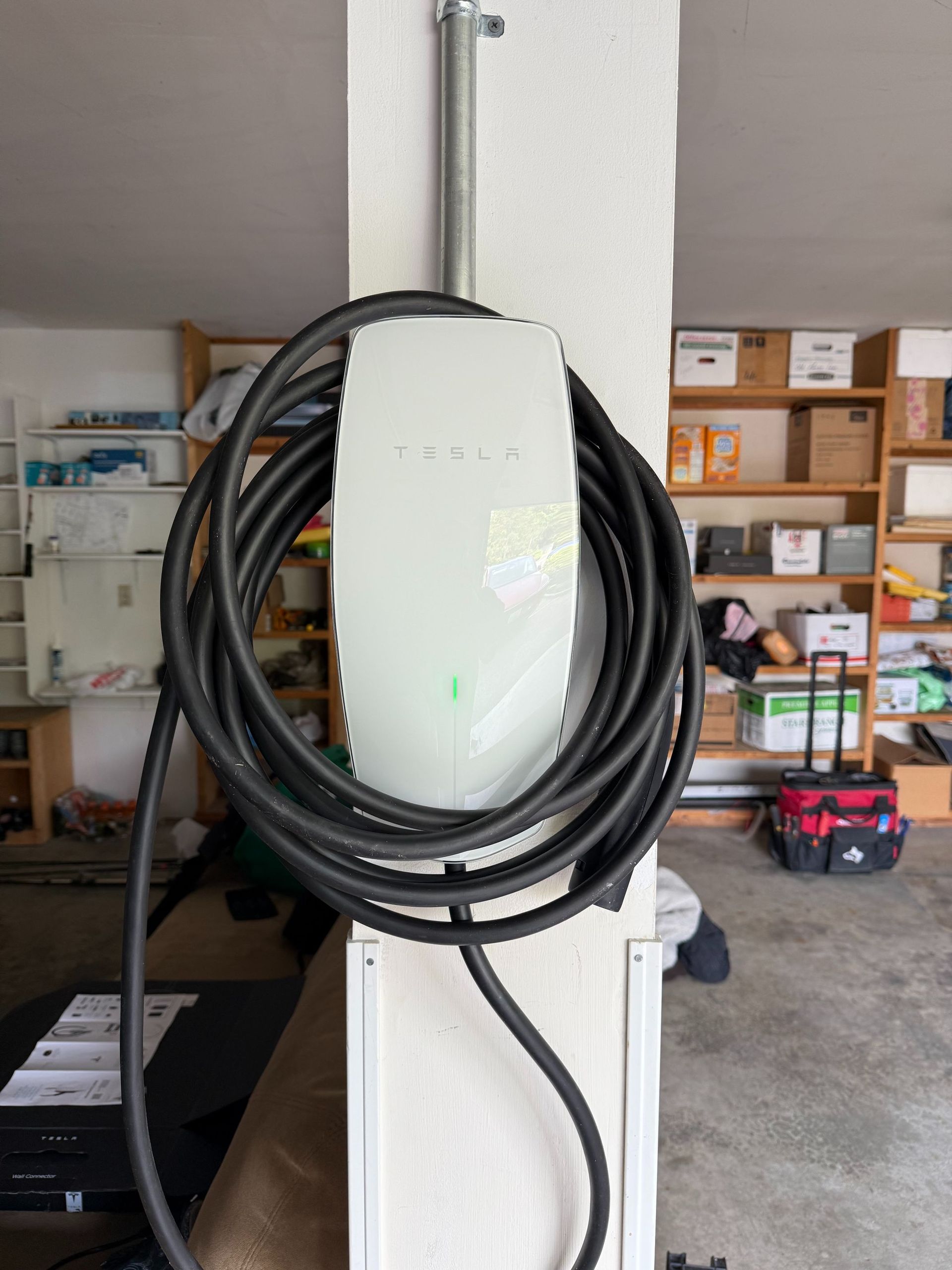 Coiled black cable hanging on a white utility post in a garage, with shelves and boxes in the background