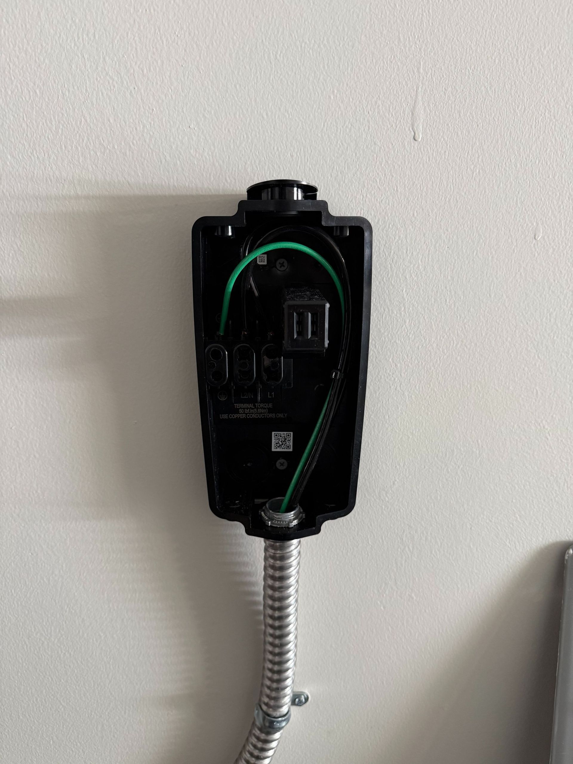 Black wall-mounted electrical device with green accents and a metal conduit on a white wall