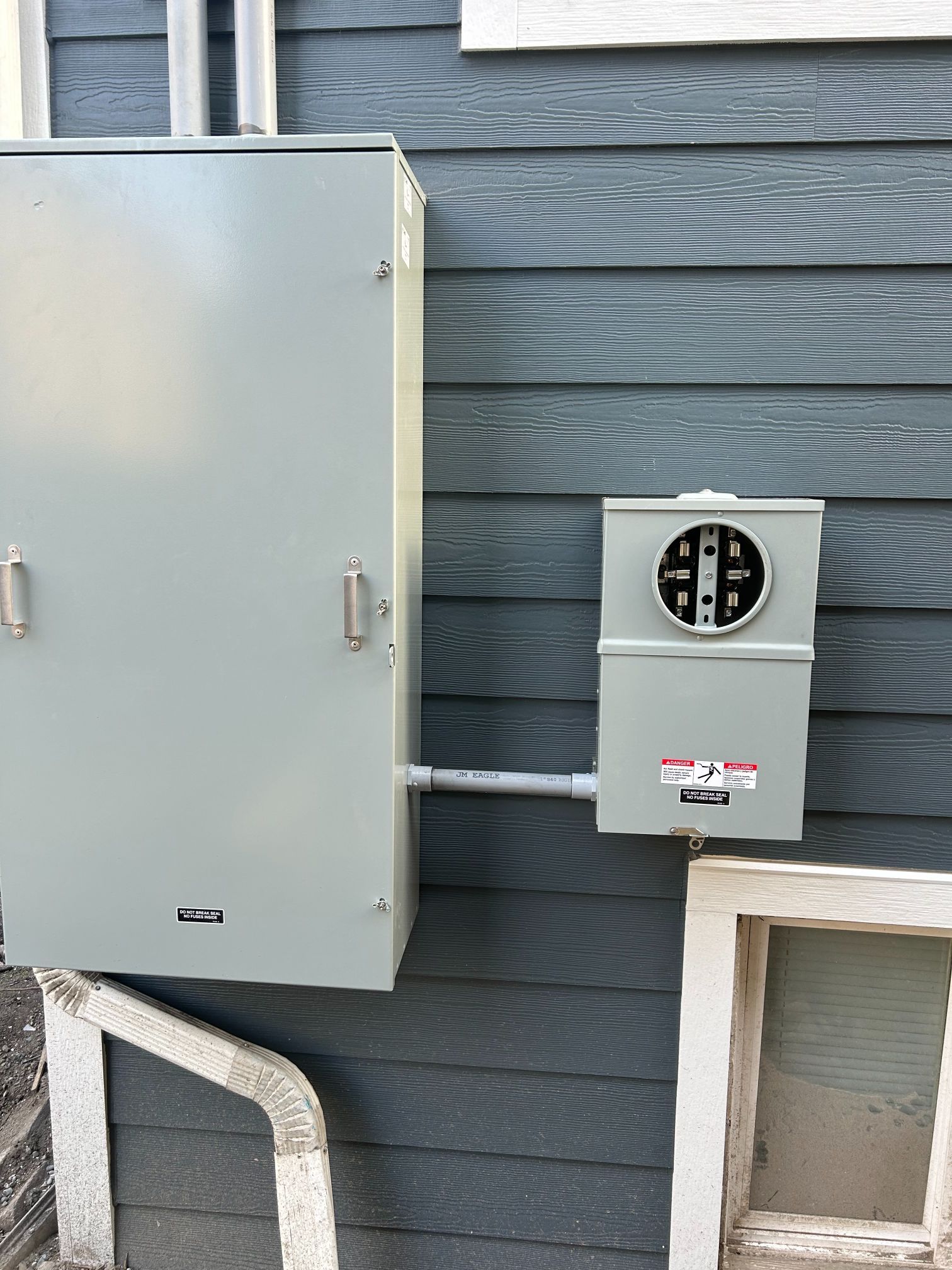 Gray electrical panels and a utility meter mounted on a blue house exterior wall.