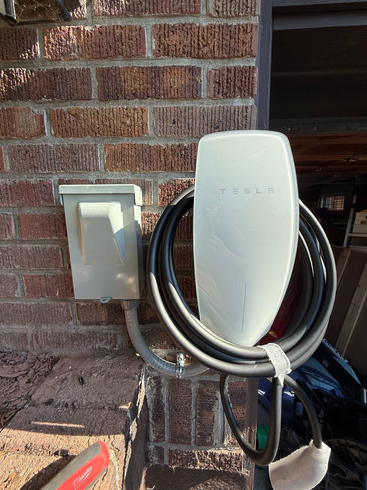 Tesla wall charger mounted on a brick exterior wall with coiled charging cable