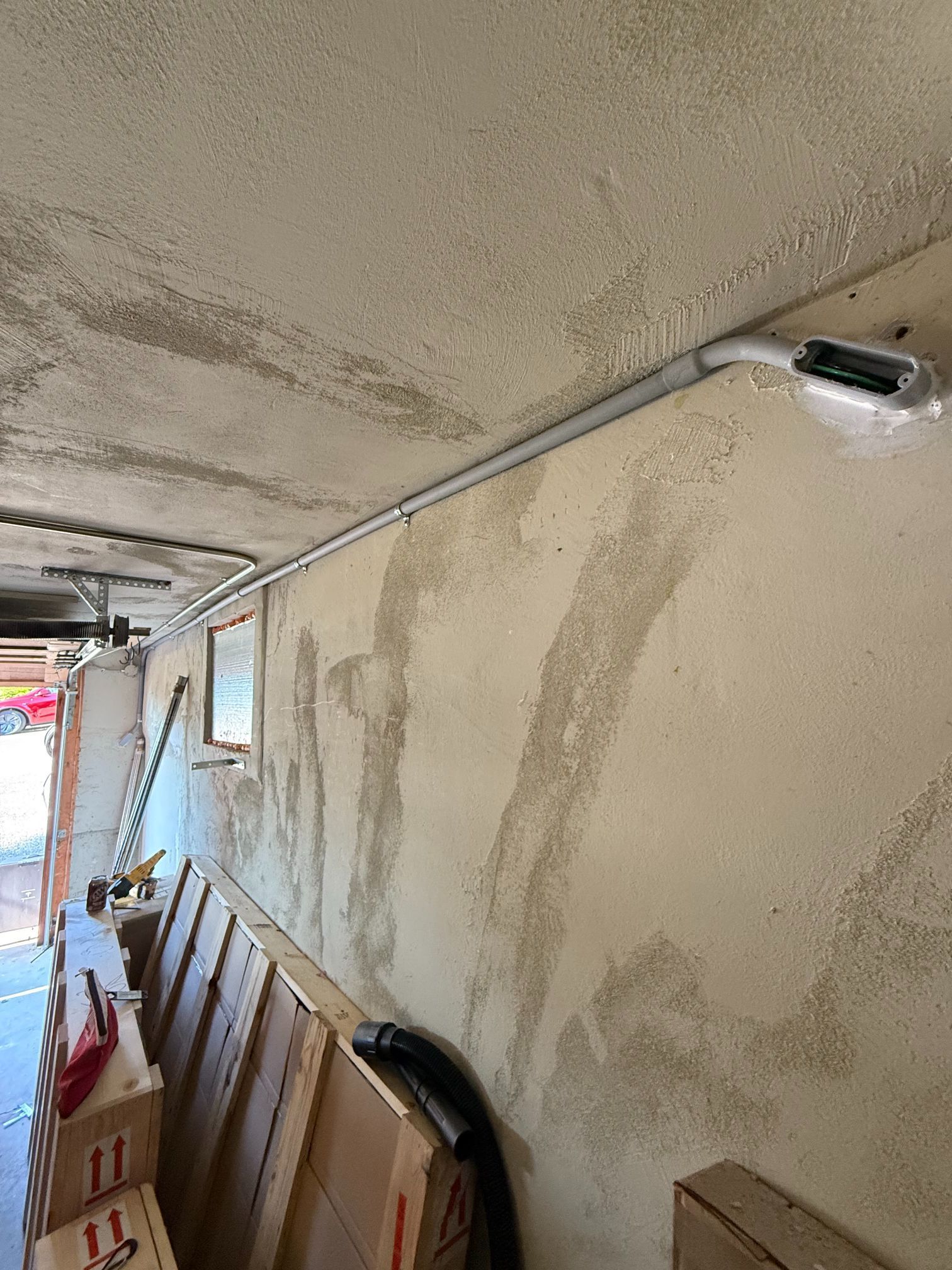 Long narrow hallway with peeling beige walls, exposed conduit, and stacked boards leaning against the side.