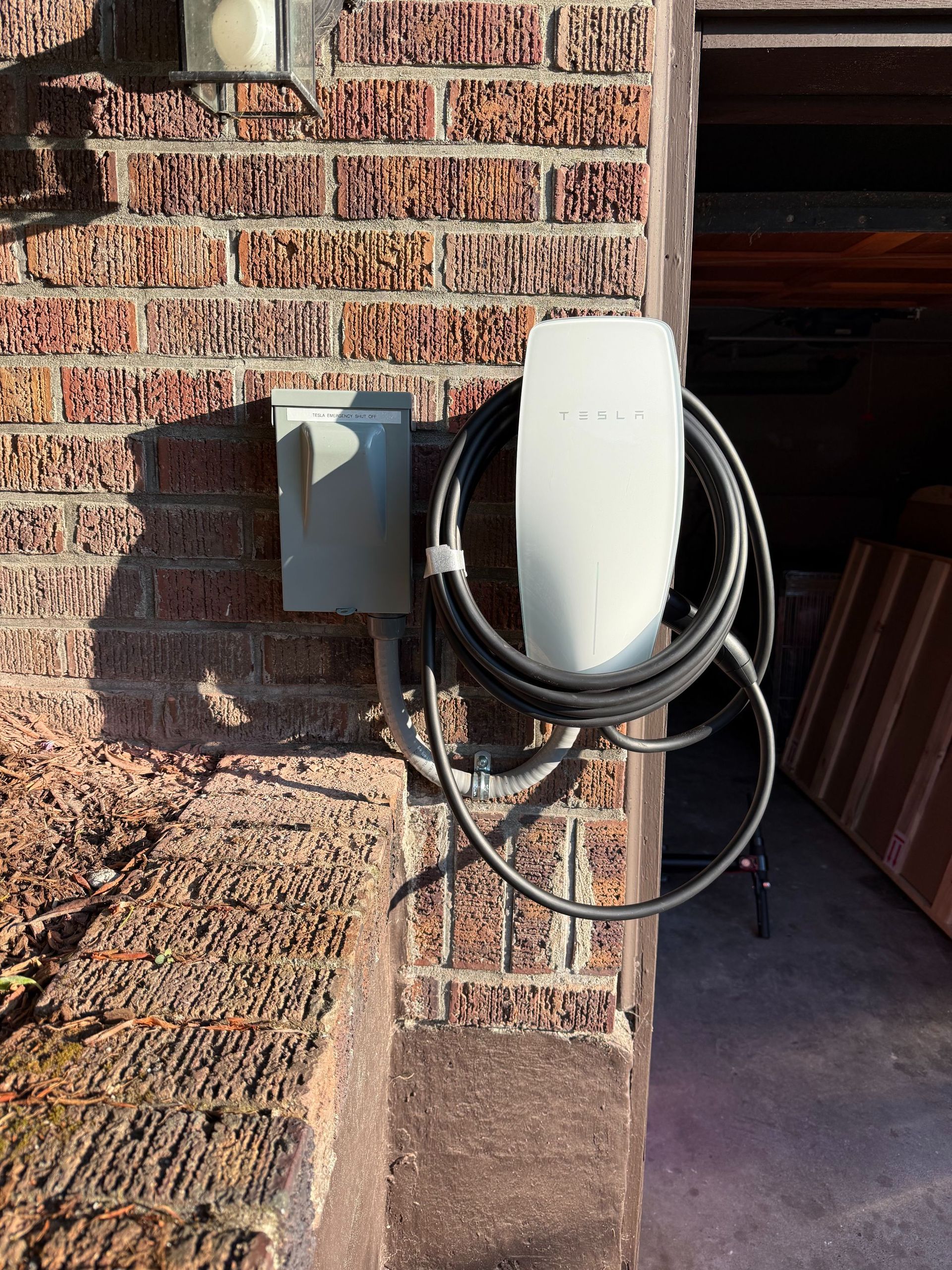 White wall-mounted EV charger with coiled black cable on a brick exterior wall.