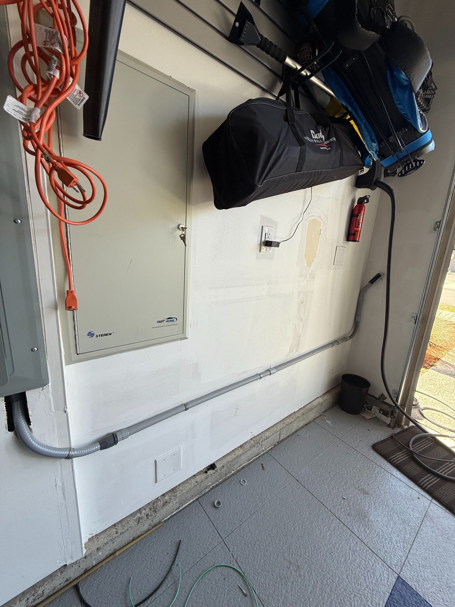 Wall-mounted utility panels and hanging cables in a garage, with a bike suspended overhead.