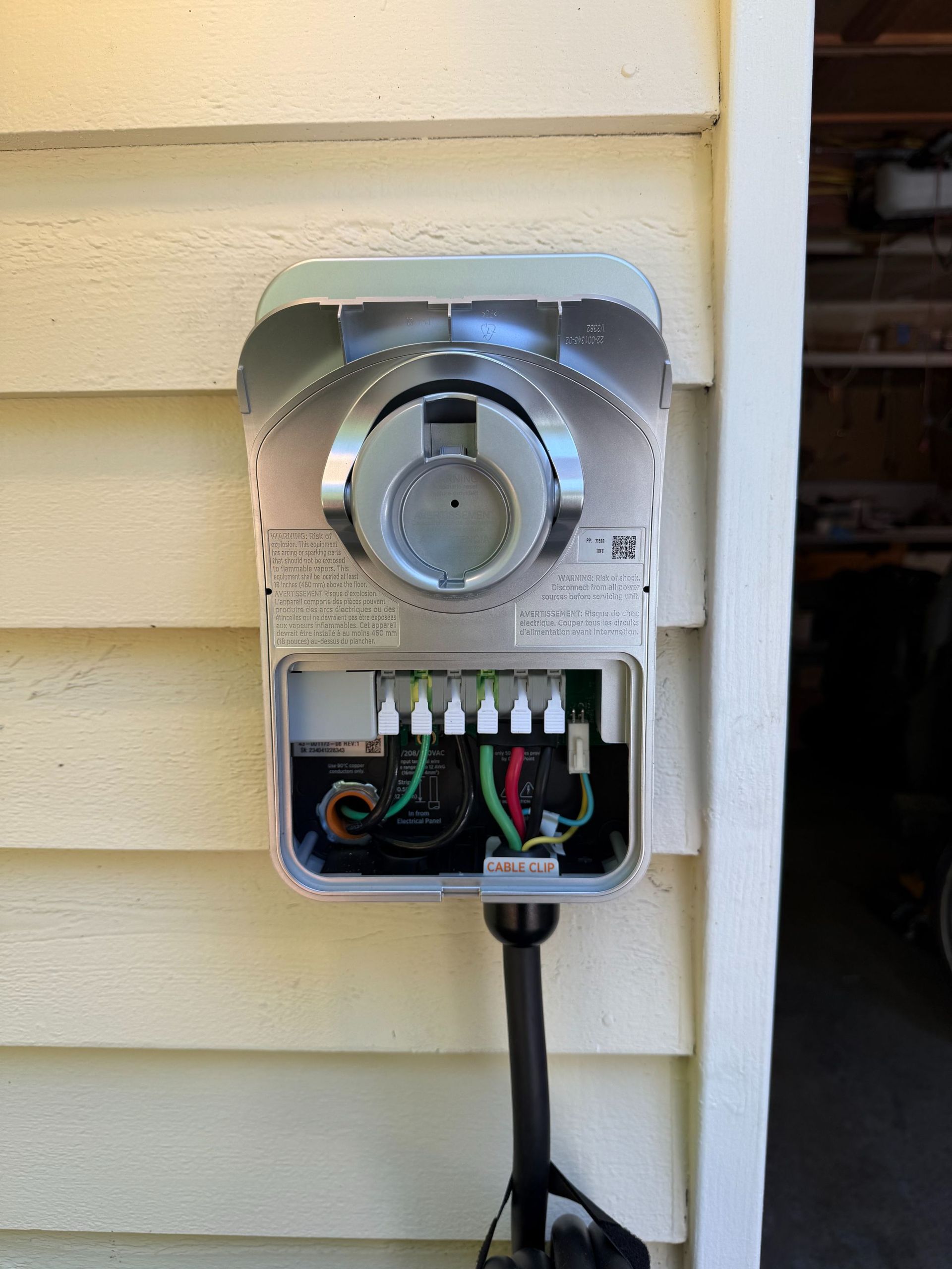 Open electrical meter panel on beige house siding with exposed wires and conduit