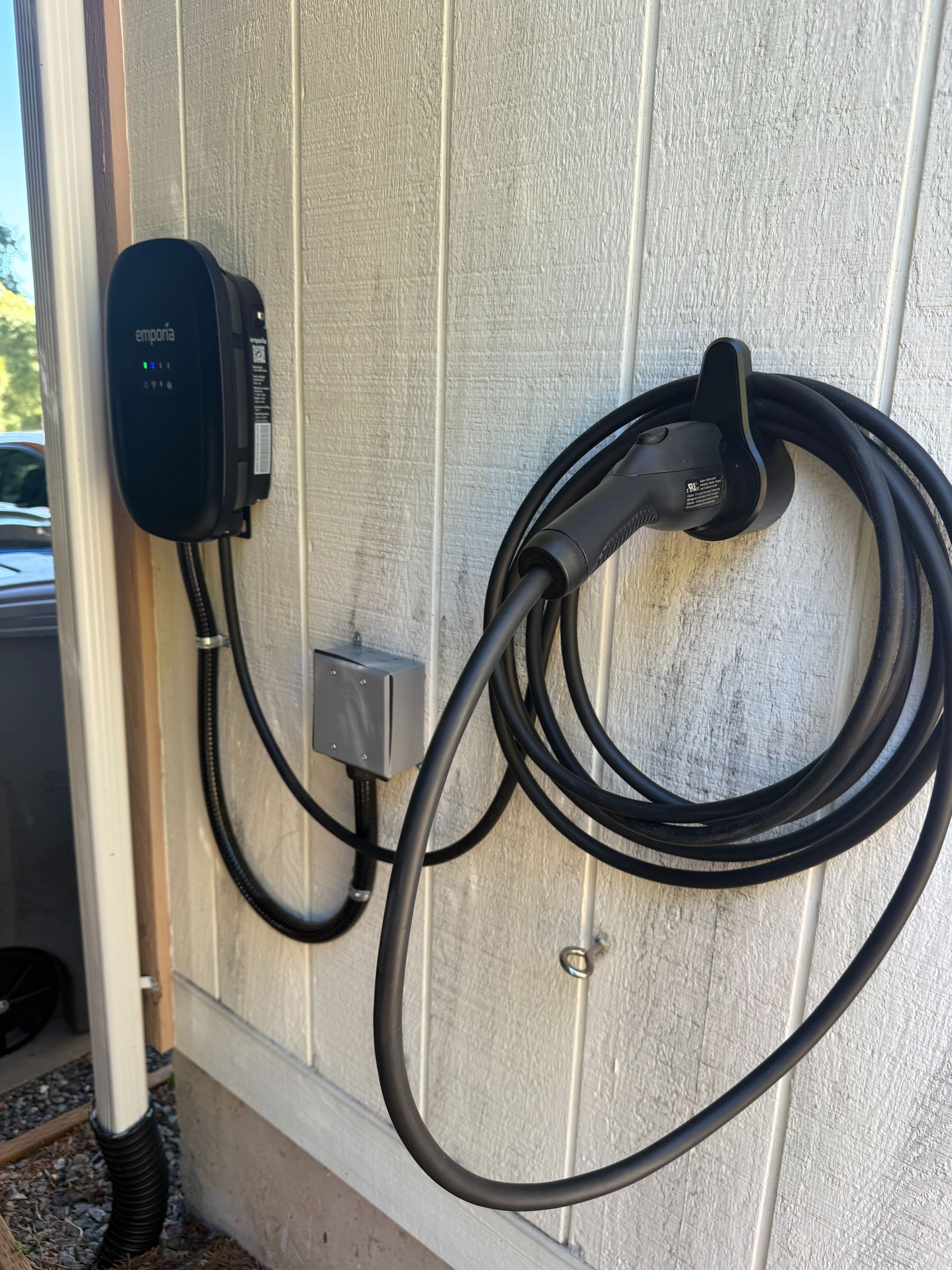 Wall-mounted electric vehicle charger with coiled cable beside a garage opening