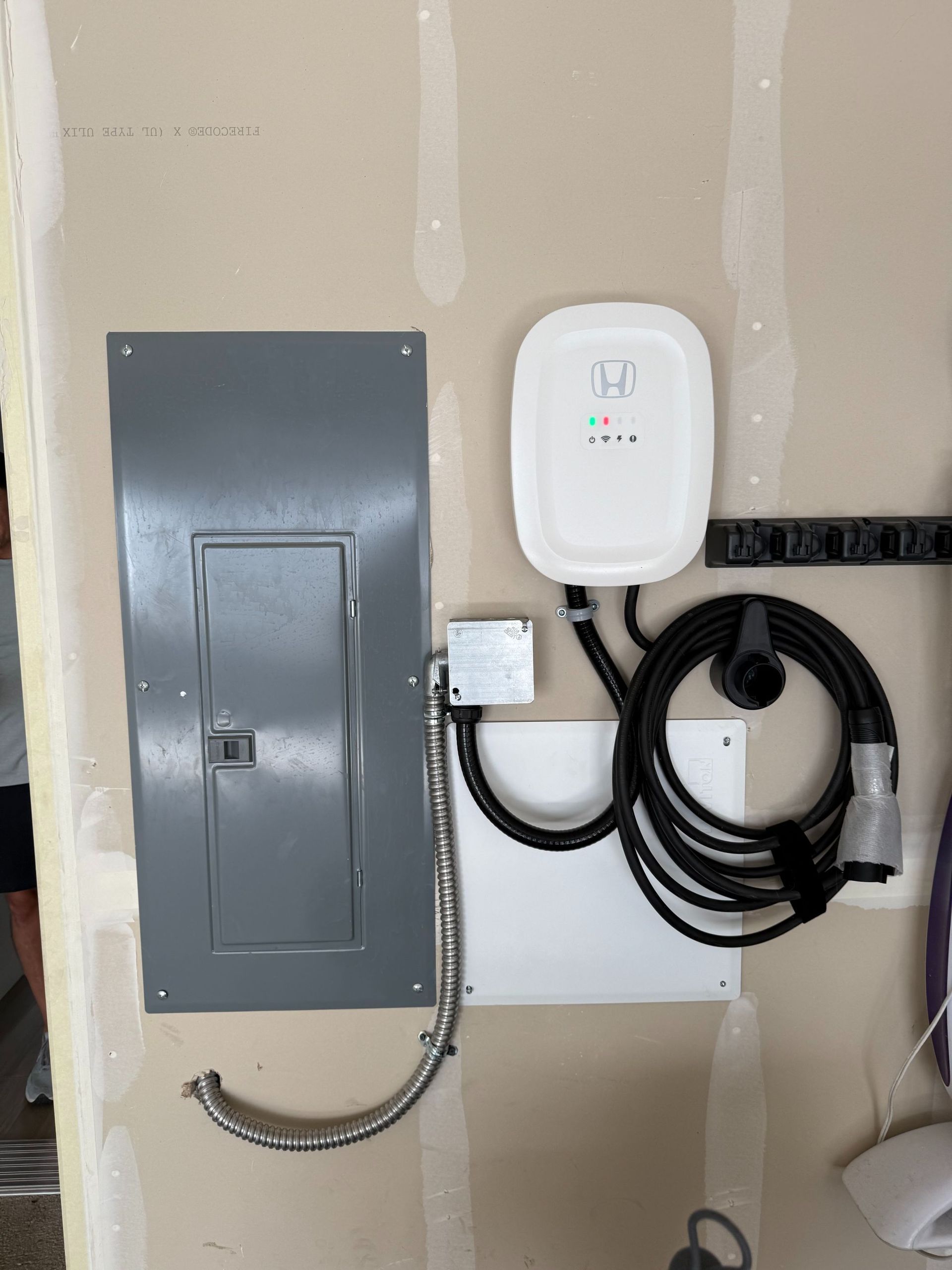 Electrical panel and EV charger mounted on unfinished wall, with coiled charging cable.