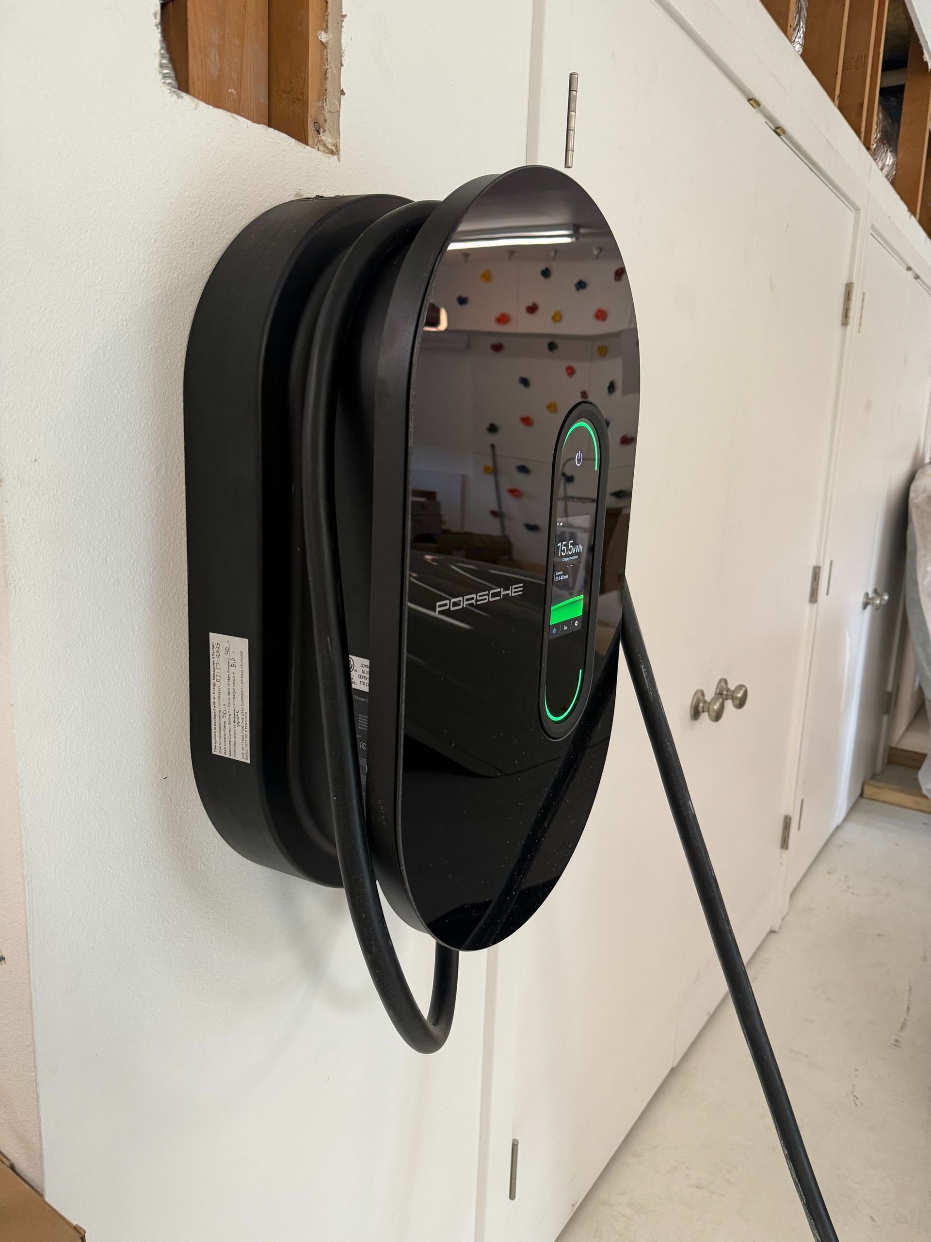 Black wall-mounted EV charger with coiled cable beside a cabinet.